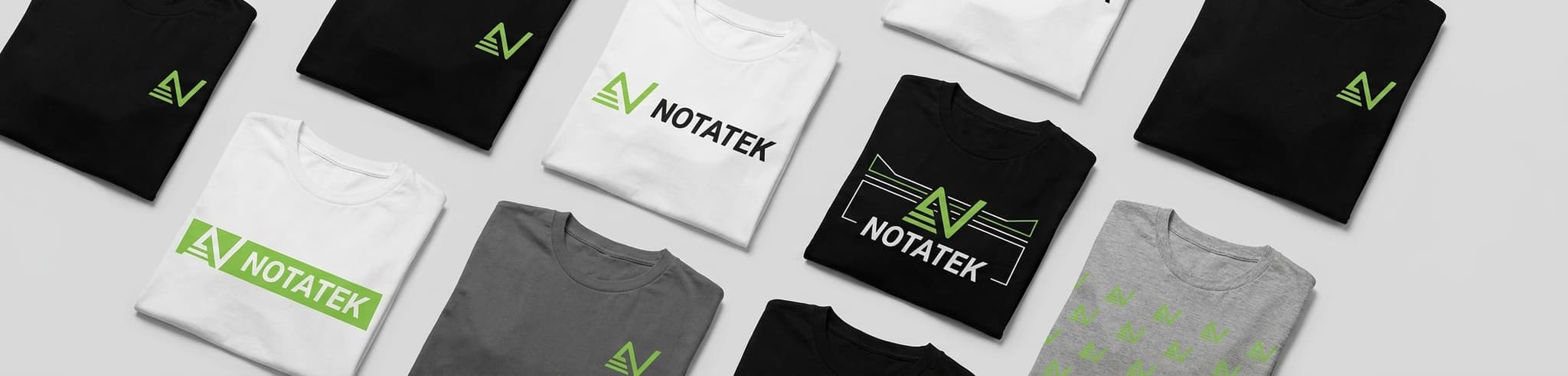 Multiple folded black, white, and grey t-shirts featuring variations of a green 'AN' logo and 'NOTATEK' text.