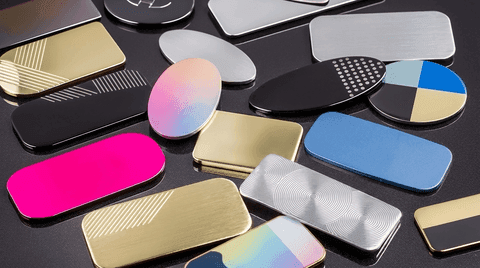 A variety of blank metallic, engraved, and brightly colored oval and rectangular name tags arranged on a dark surface.