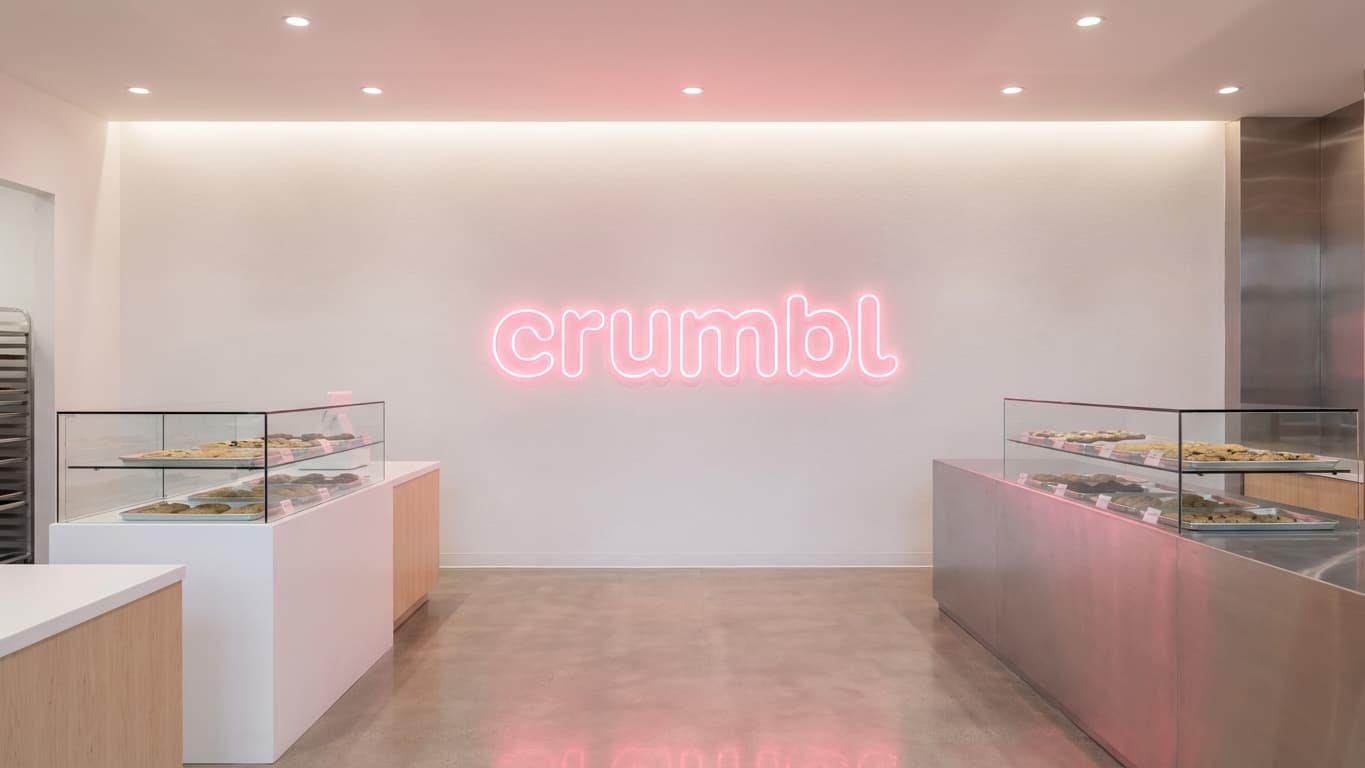 A modern Crumbl cookies store interior featuring a large pink illuminated sign on the wall.