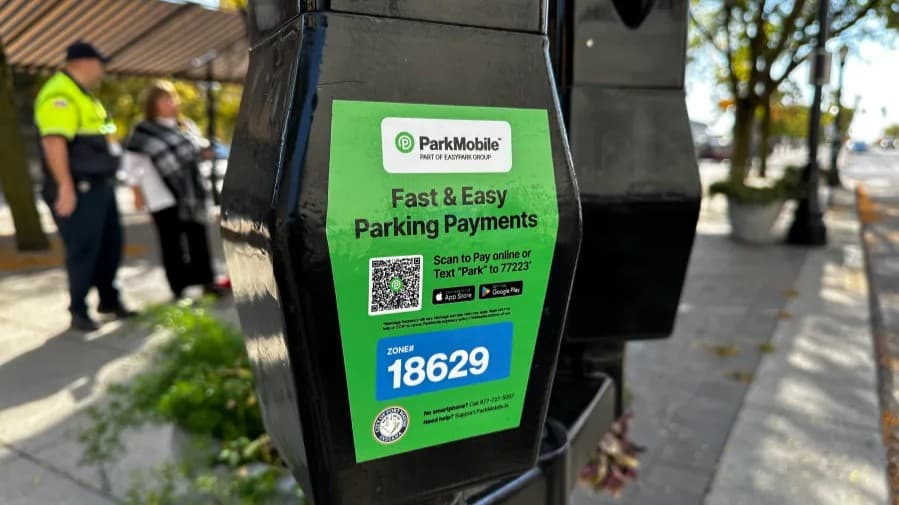 Close-up of a ParkMobile QR code sticker applied to a black parking meter in an urban setting.