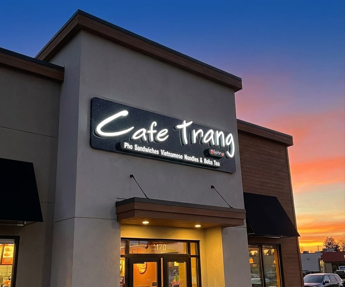 Illuminated Cafe Trang Bistro storefront sign against a sunset sky.