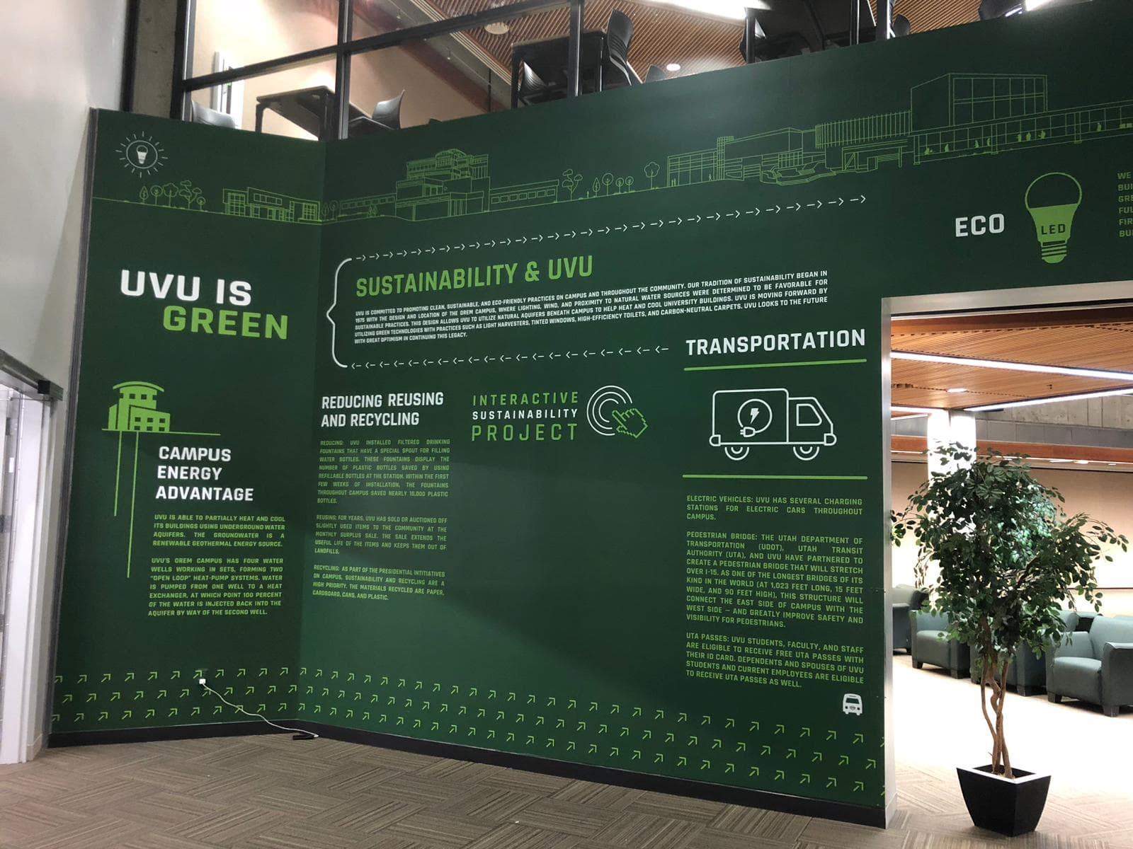Green interior wall graphic at Utah Valley University displaying campus sustainability initiatives and eco-friendly stats.