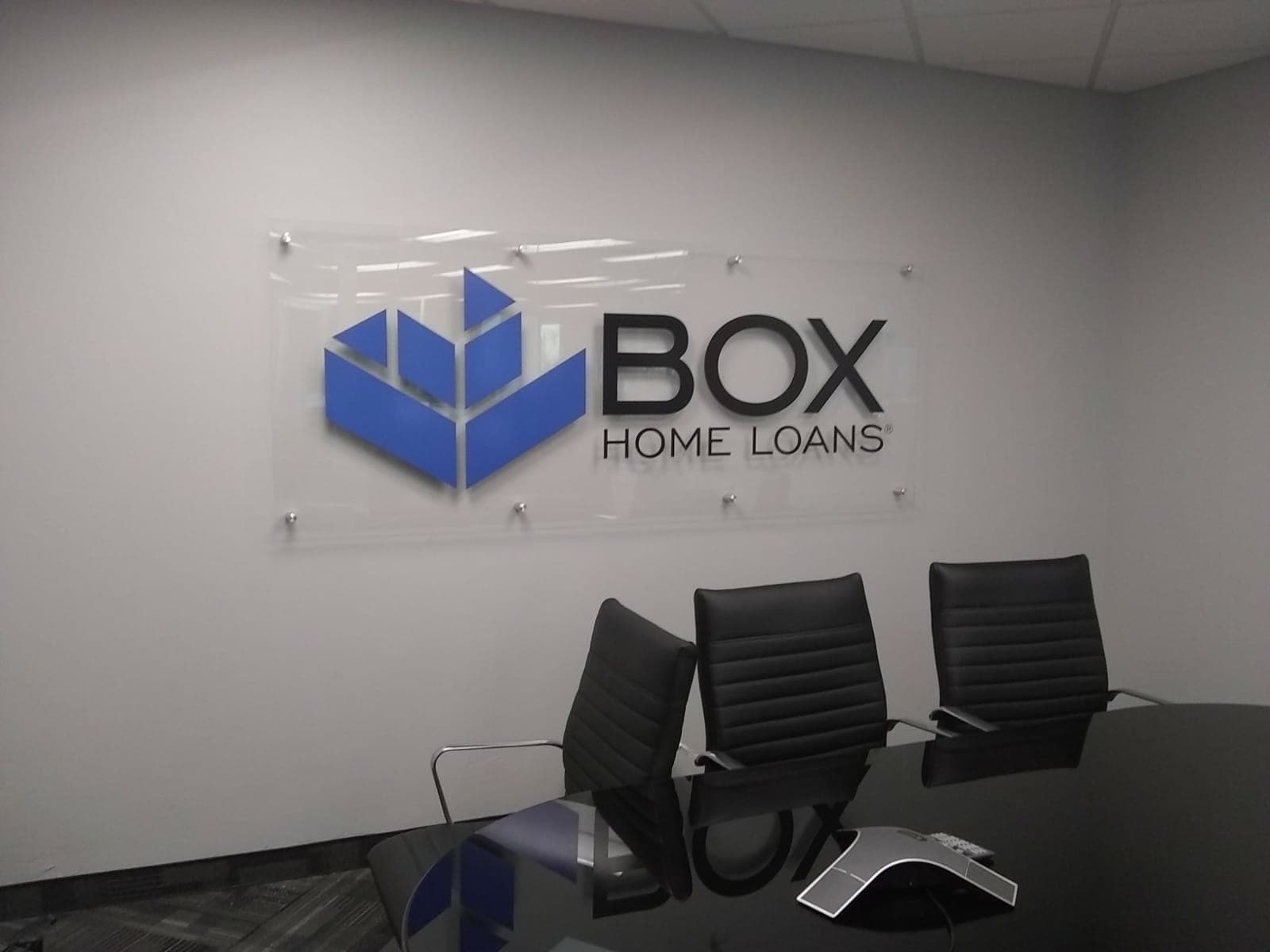 Acrylic Box Home Loans lobby sign mounted on a wall above a conference table.