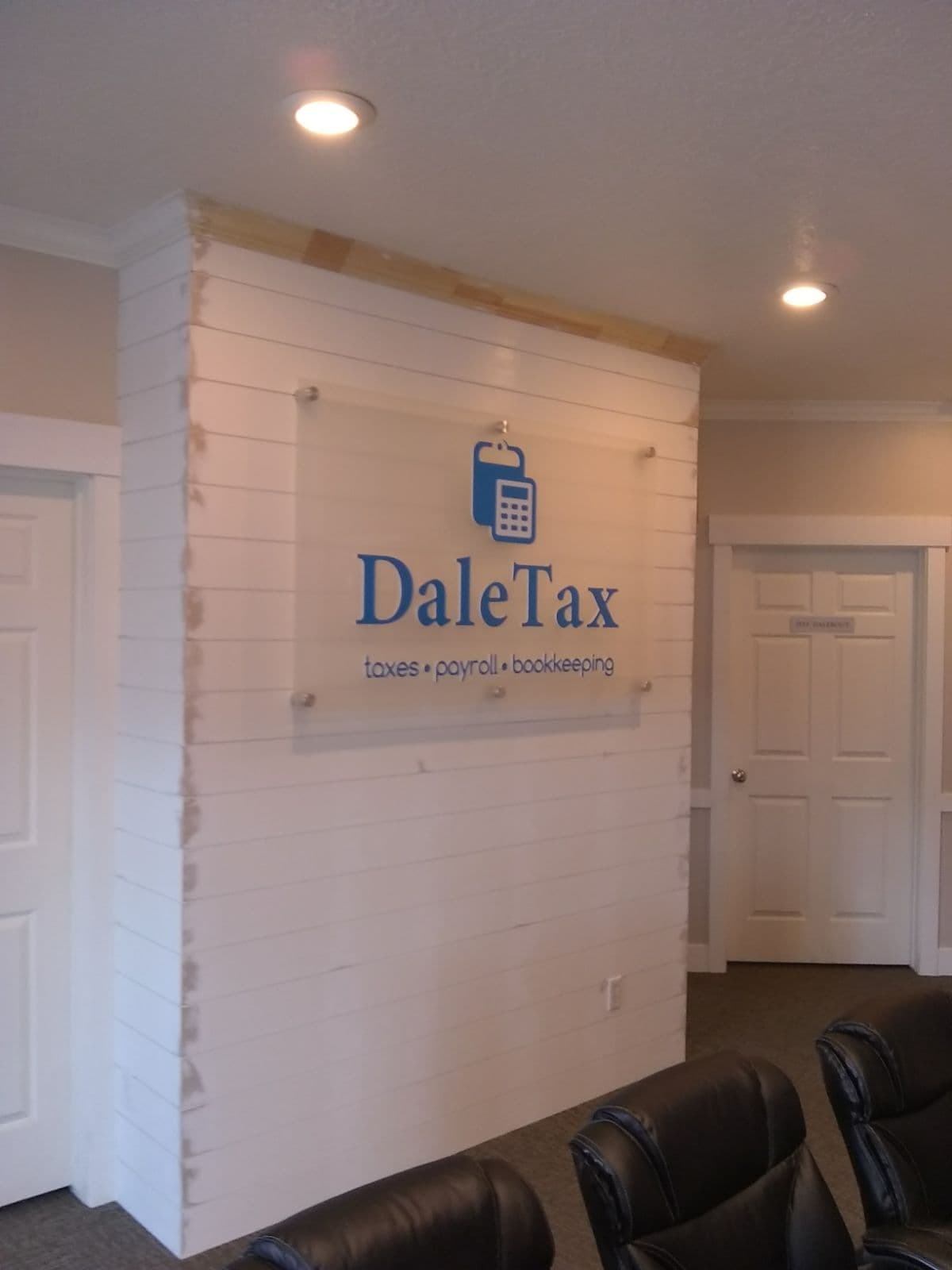 Acrylic DaleTax lobby sign mounted with standoffs on a white shiplap wall in an office reception area.