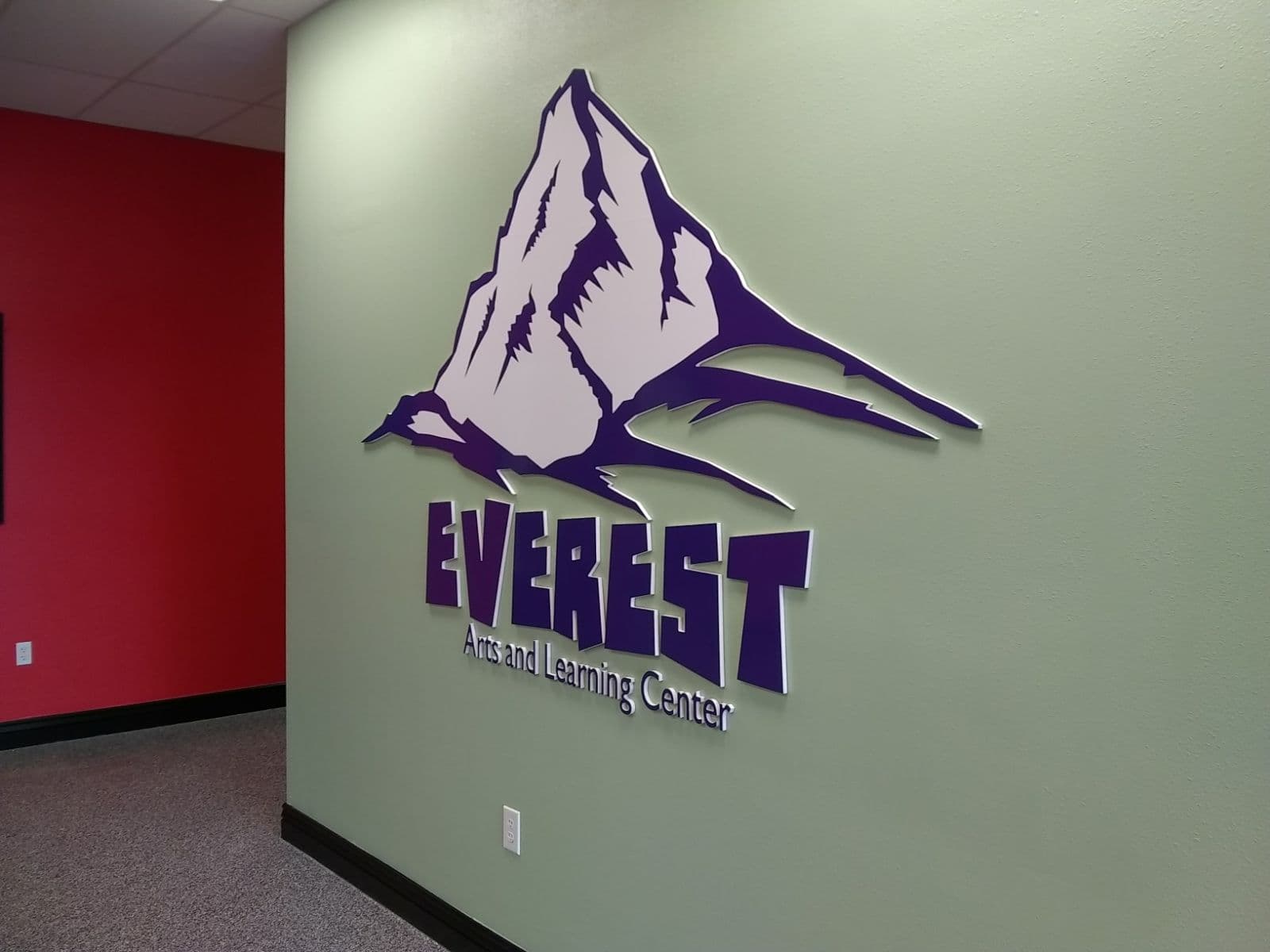 Dimensional purple mountain logo and lettering for Everest Arts and Learning Center on a light green wall.
