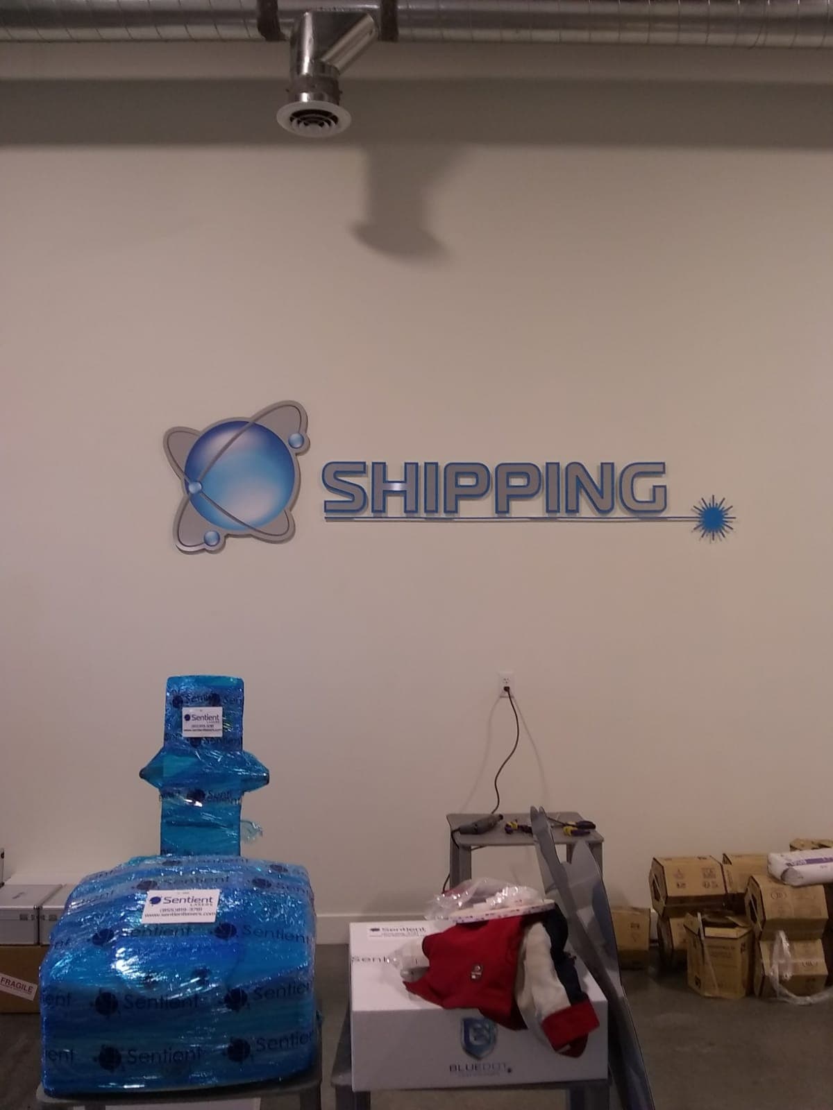 Blue and silver dimensional wall sign reading SHIPPING mounted in a commercial shipping department.