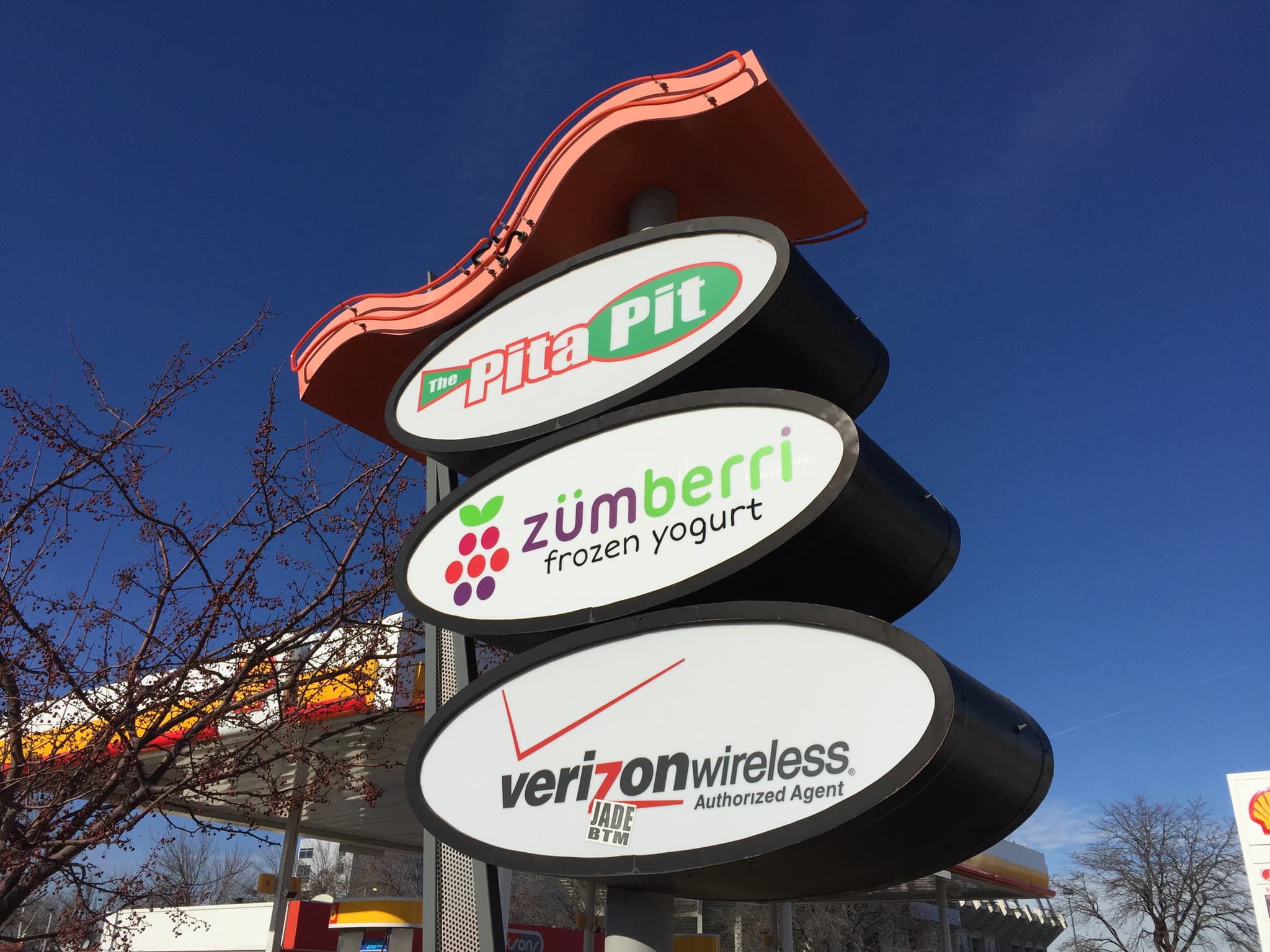 Multi-tenant outdoor pylon sign featuring illuminated logos for Pita Pit, Zumberri Frozen Yogurt, and Verizon Wireless.