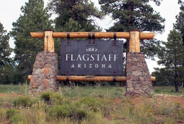 Rustic wooden and stone welcome sign displaying 1882 Flagstaff Arizona in a forest setting.