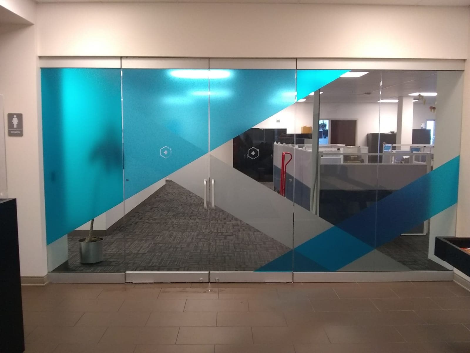 Glass office double doors decorated with geometric teal, blue, and gray frosted vinyl decals.