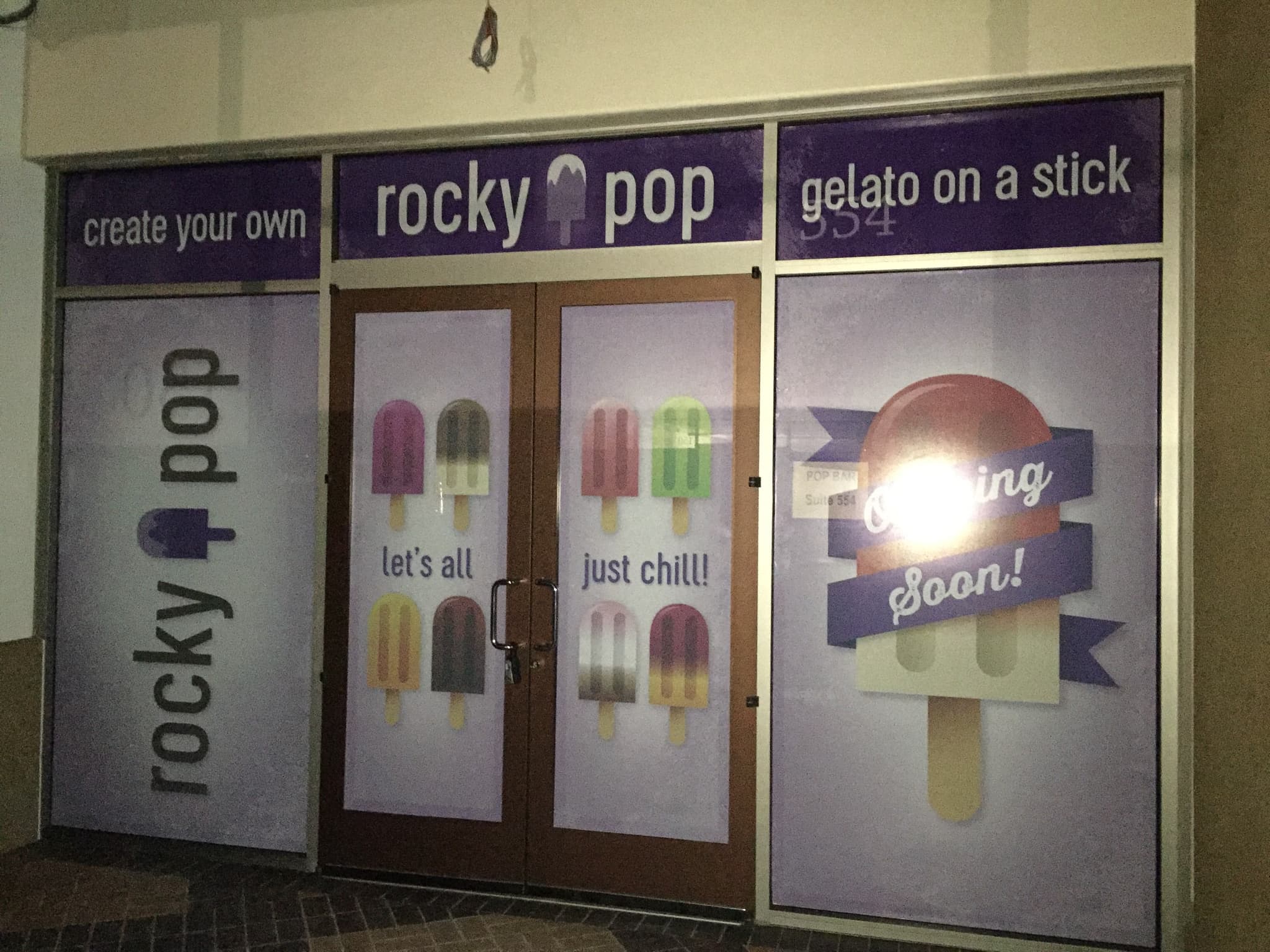 Storefront decorated with purple Rocky Pop window graphics announcing gelato on a stick coming soon.