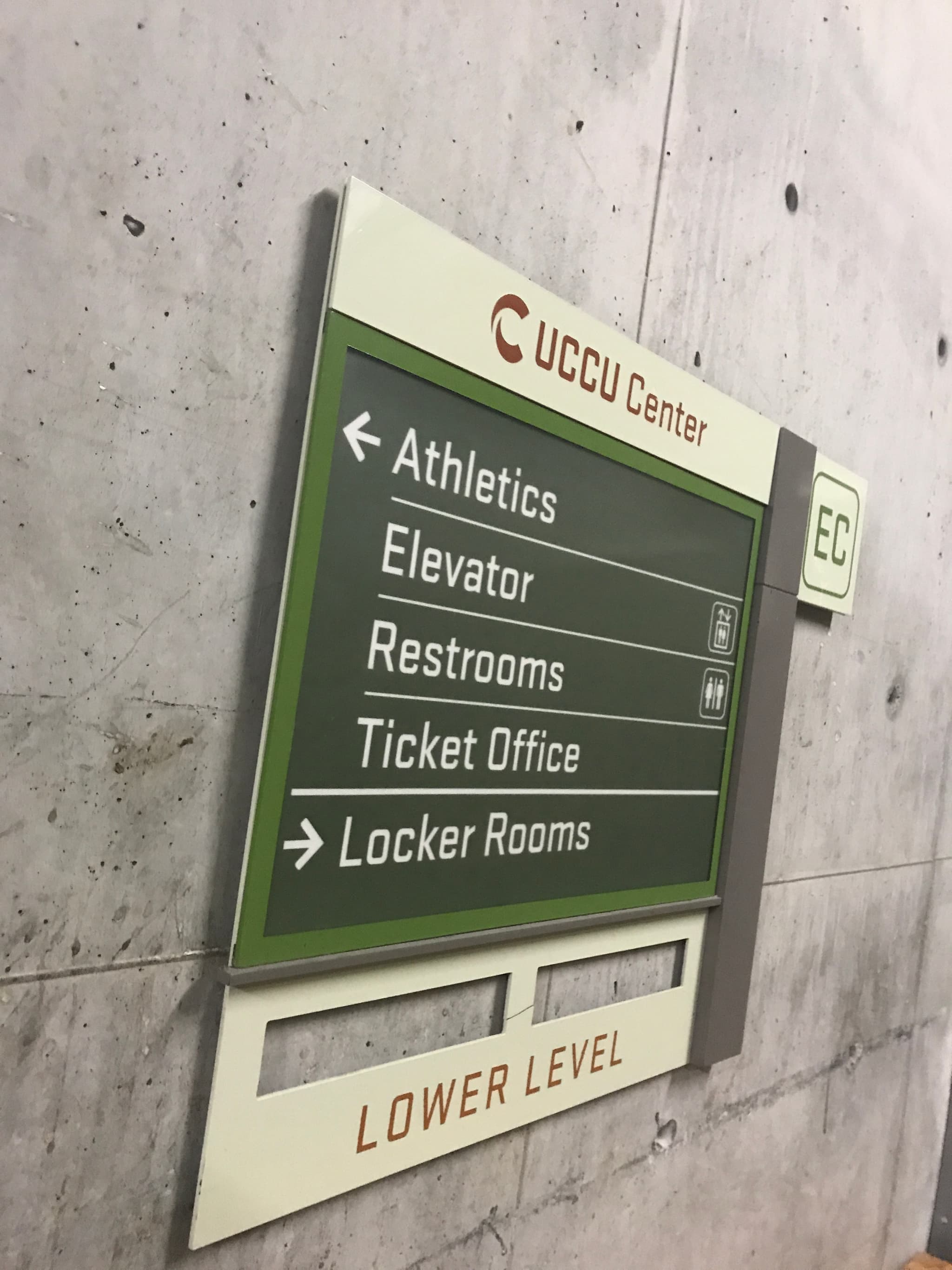 Directional wayfinding sign mounted on a concrete wall inside the UCCU Center at Utah Valley University.