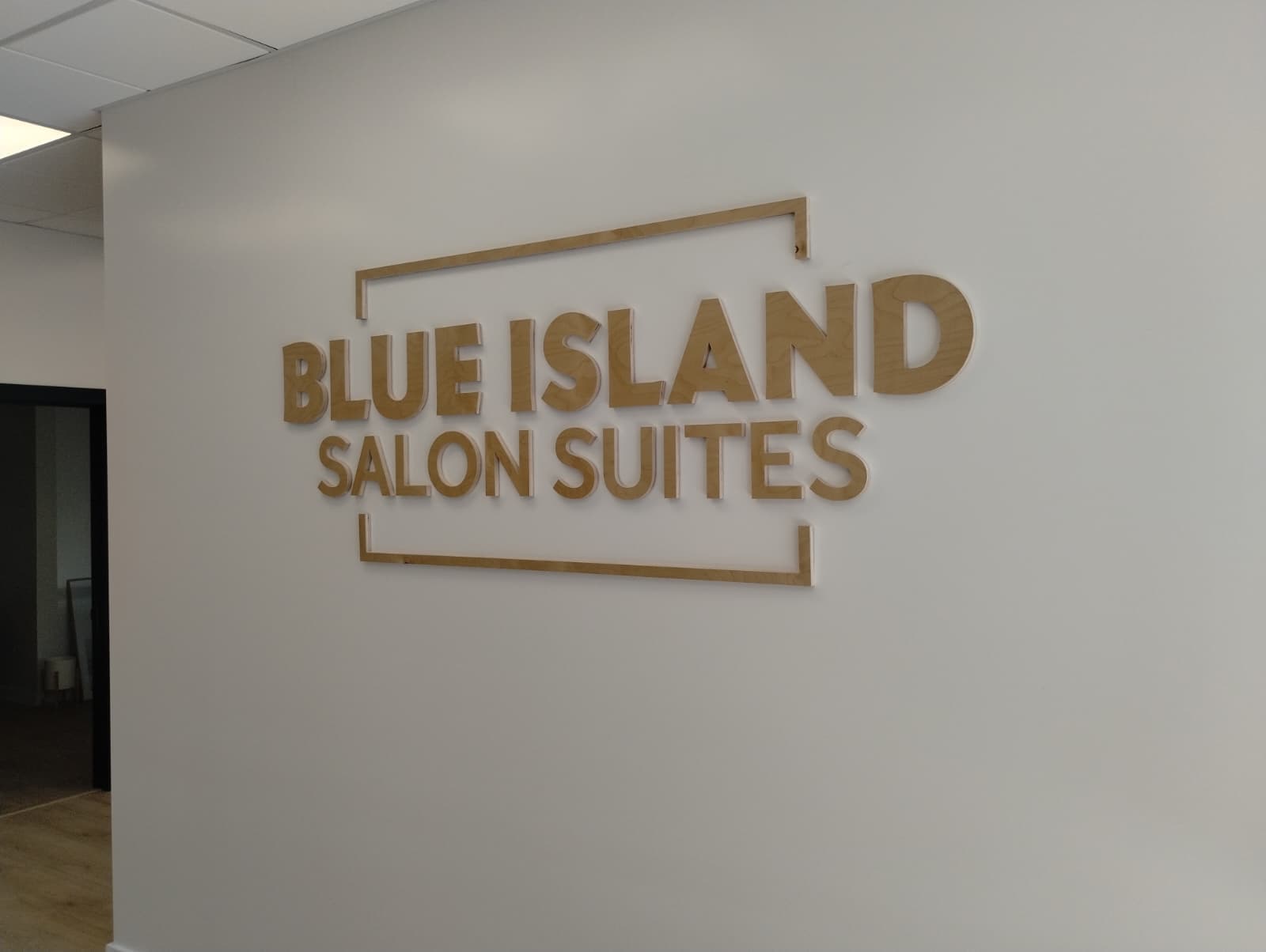 Wooden dimensional lobby sign reading Blue Island Salon Suites mounted on a white wall.