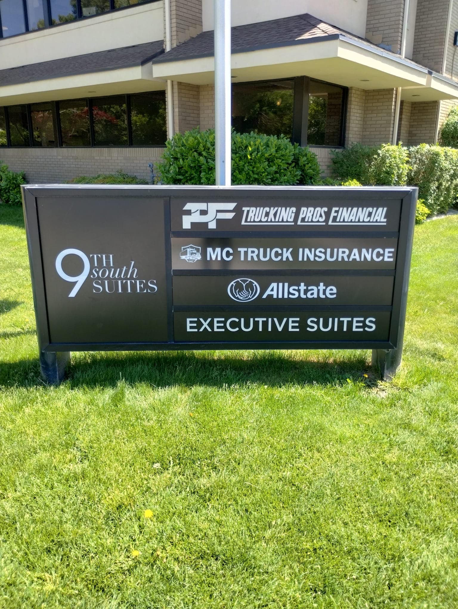Black monument directory sign for 9th South Suites situated on a grassy lawn in front of an office building.