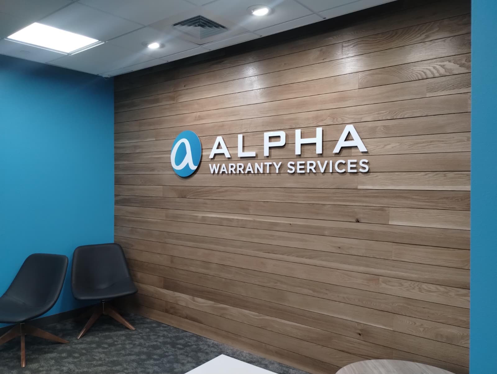 Alpha Warranty Services dimensional lobby sign mounted on a wood plank wall in an office reception area.