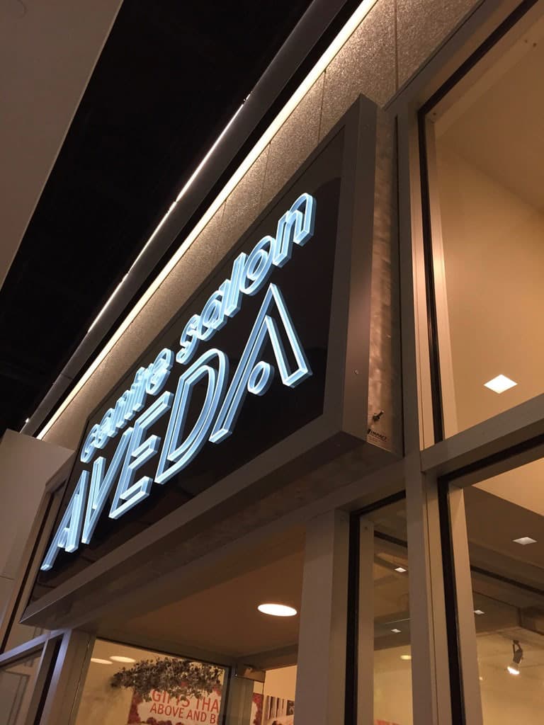 Illuminated white electric sign for Centre Salon Aveda mounted above a glass storefront.