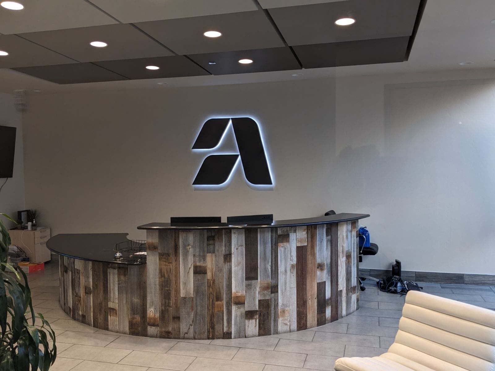 Halo-lit Artemis Health logo mounted behind a curved reclaimed wood reception desk in an office lobby.