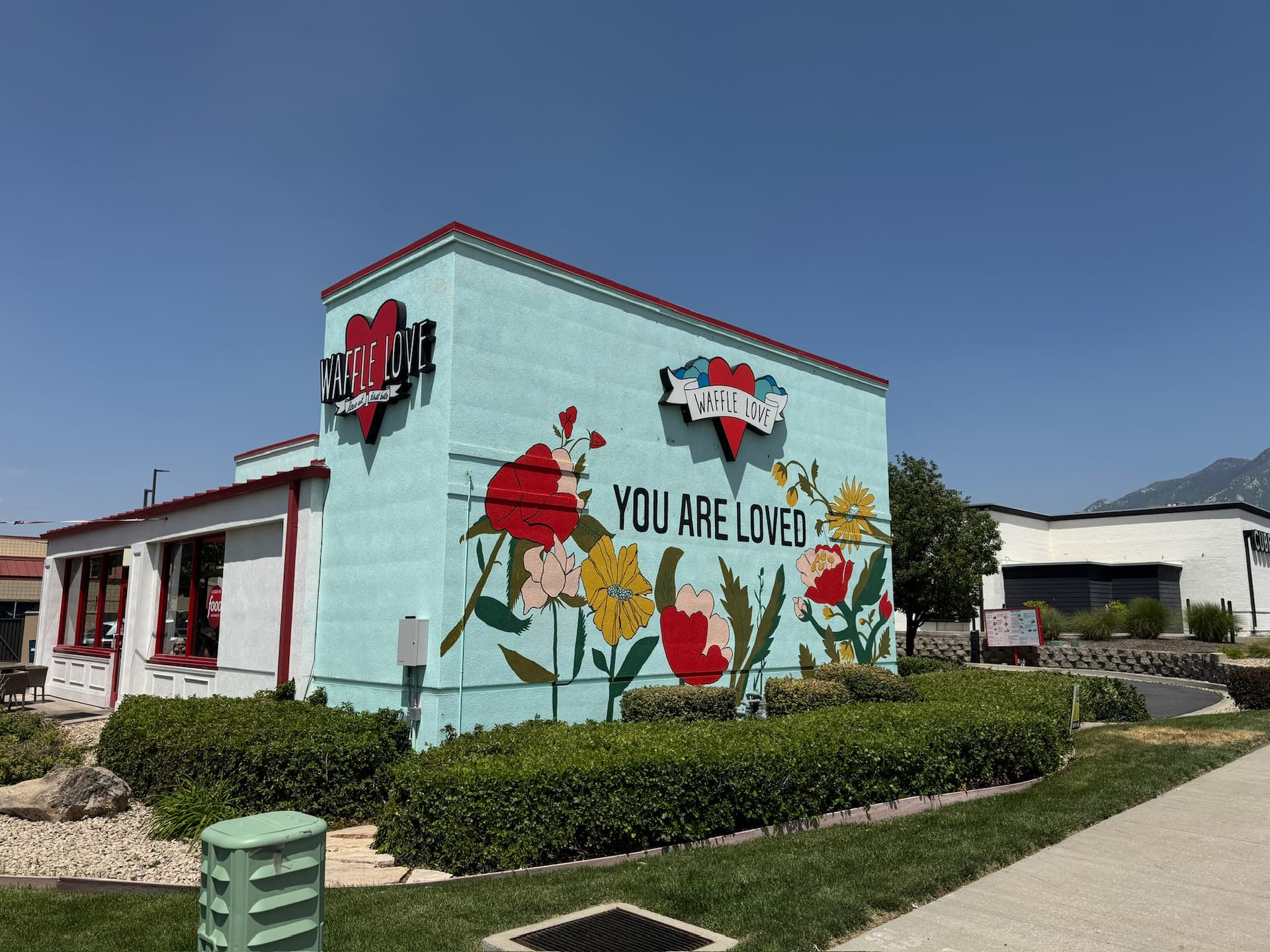 Light blue Waffle Love building featuring custom dimensional signage and a floral mural reading 'You Are Loved'.