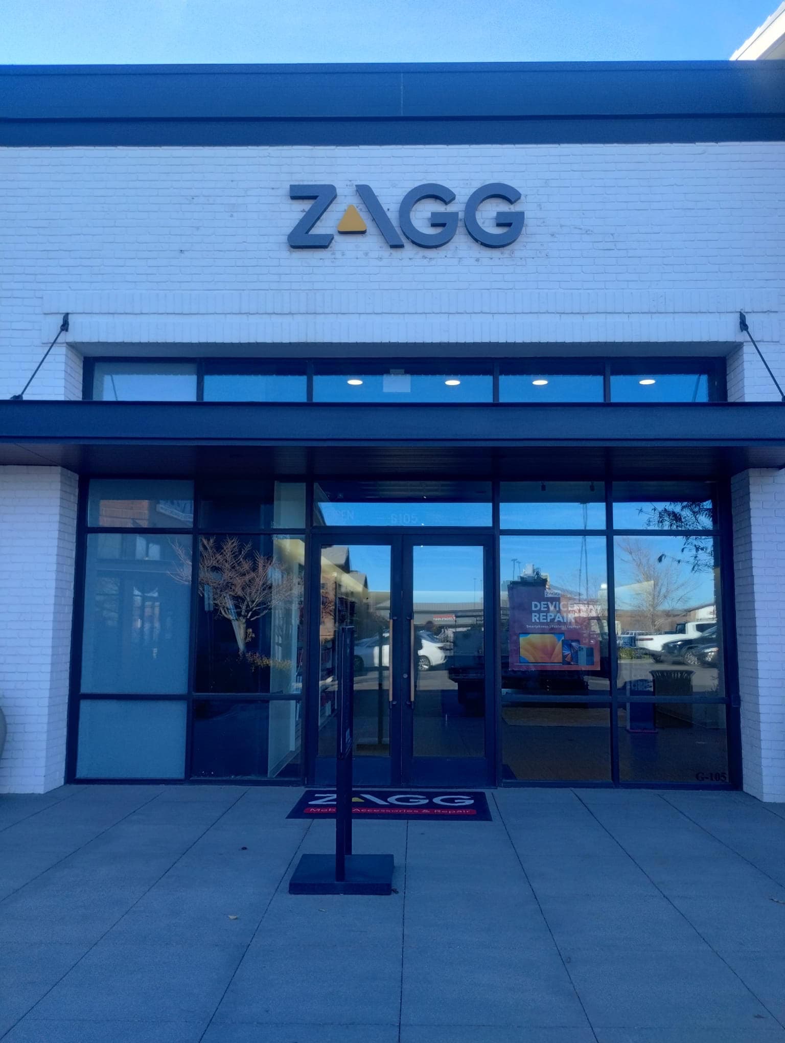 Exterior view of a ZAGG store with black dimensional logo signage mounted on a white brick facade.