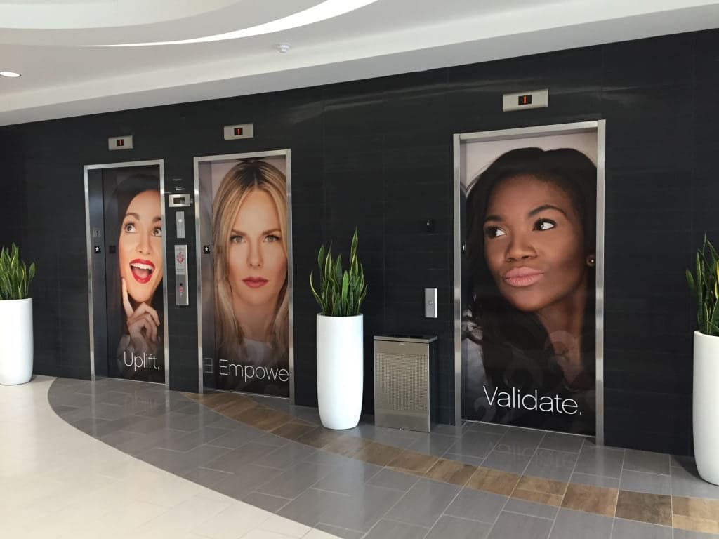 Three elevator doors wrapped with portraits of women and words Uplift, Empower, and Validate.