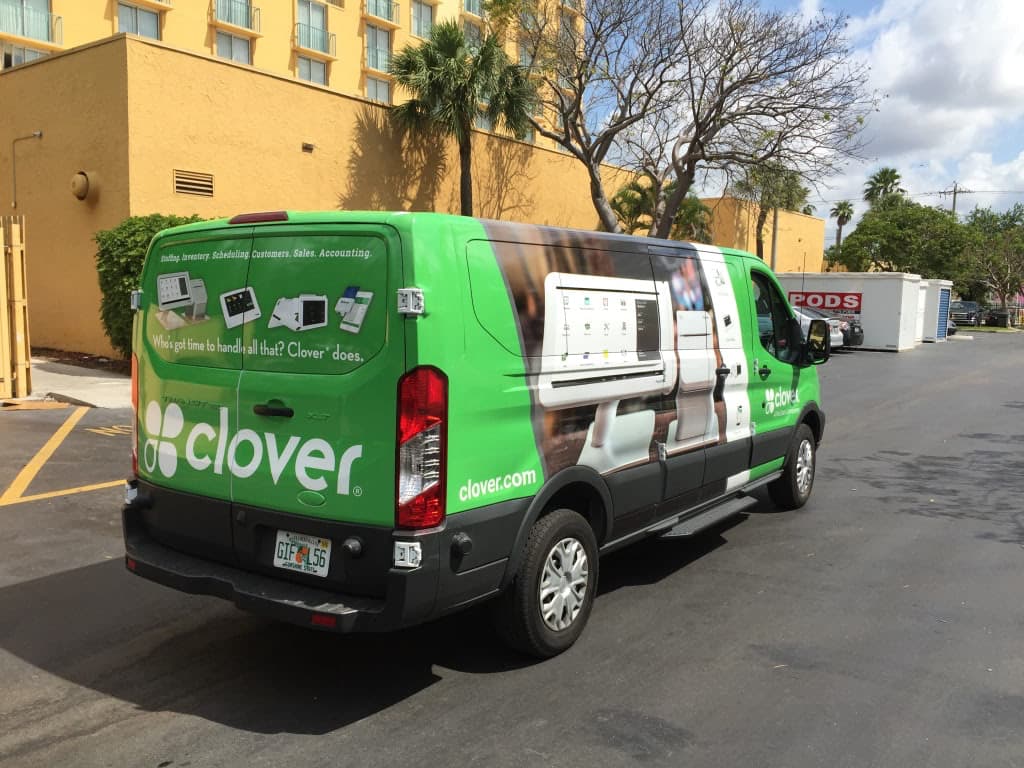 Bright green and white vehicle wrap on a Clover POS commercial van parked outdoors.