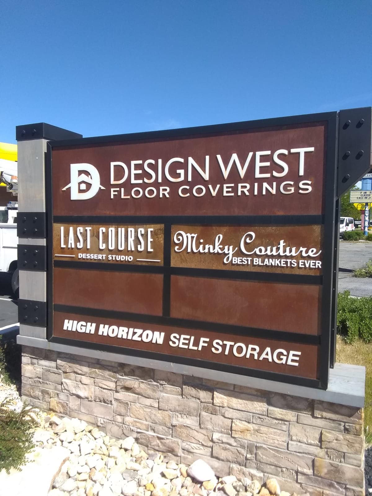 A multi-tenant outdoor monument sign featuring Design West Floor Coverings and other business logos.