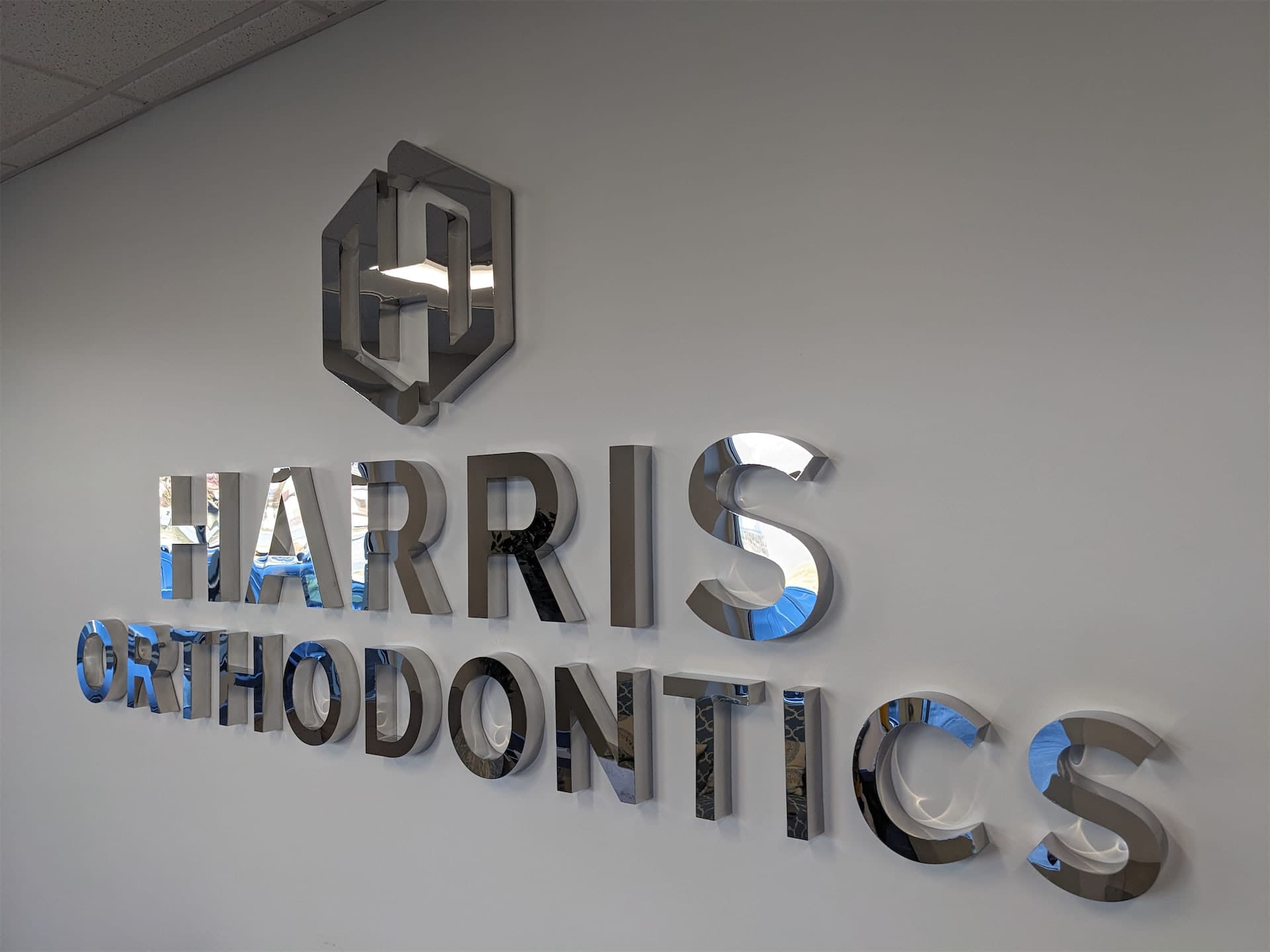 Polished chrome dimensional wall sign reading Harris Orthodontics inside an office lobby.