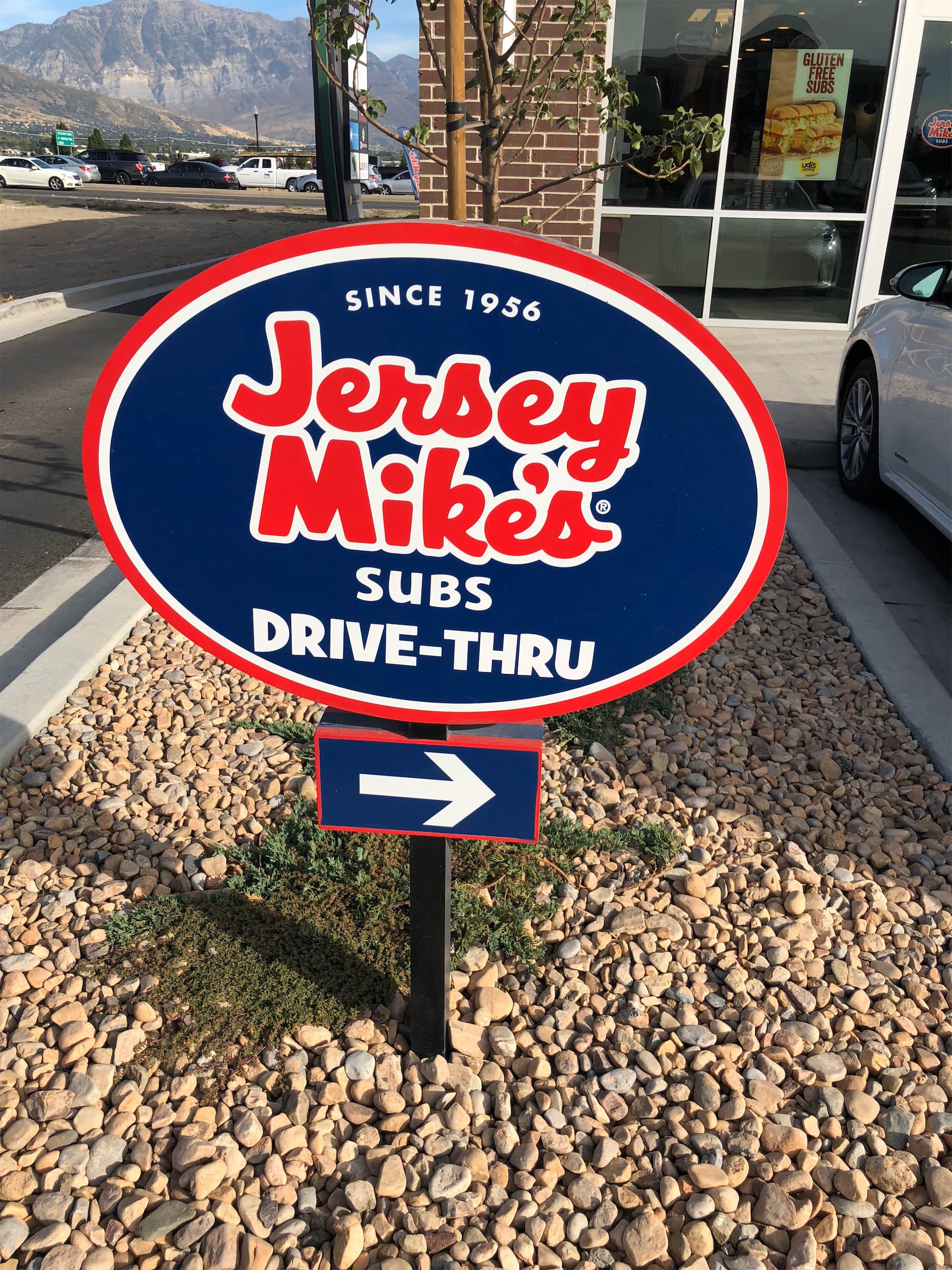 Jersey Mike's Subs drive-thru directional sign with a white right-pointing arrow set in rock landscaping.