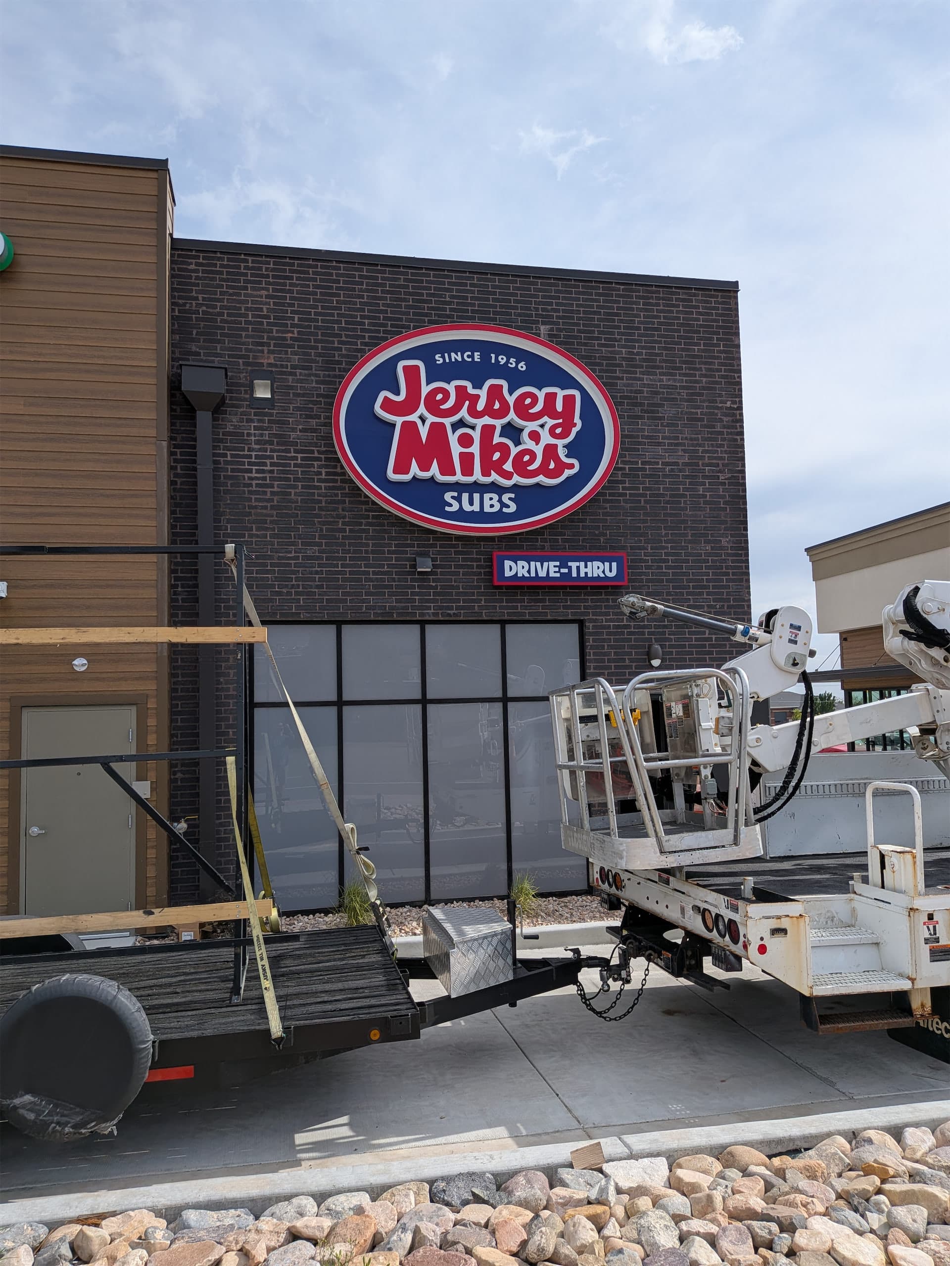 Exterior Jersey Mike's Subs illuminated sign mounted on a dark brick store facade with installation equipment.