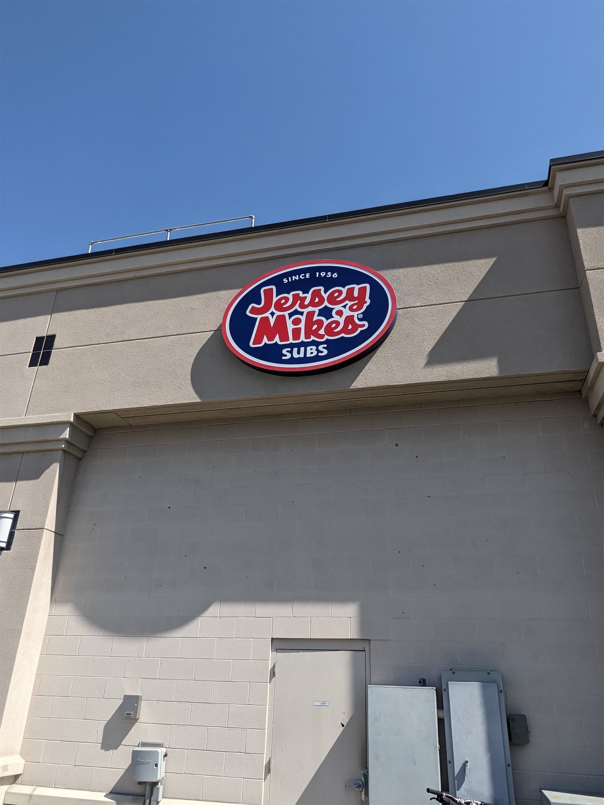 Jersey Mike's Subs oval exterior building sign mounted on a beige wall.