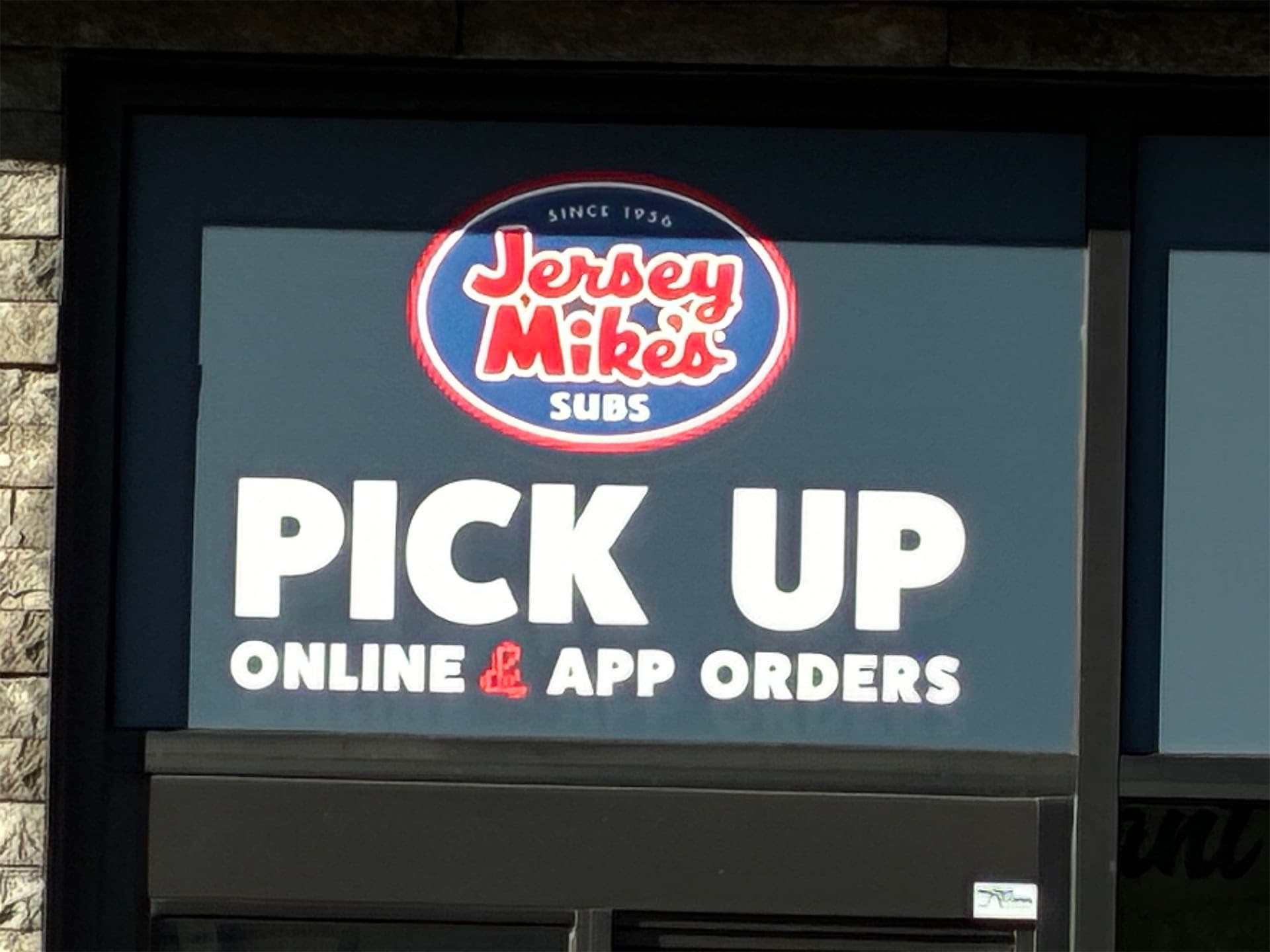 Illuminated Jersey Mike's Subs sign directing customers to pick up online and app orders.