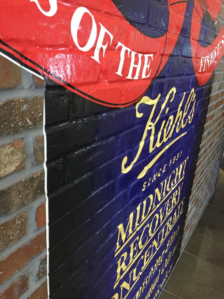 Close-up side view of a Kiehl's branded custom wall graphic applied to an interior exposed brick wall.