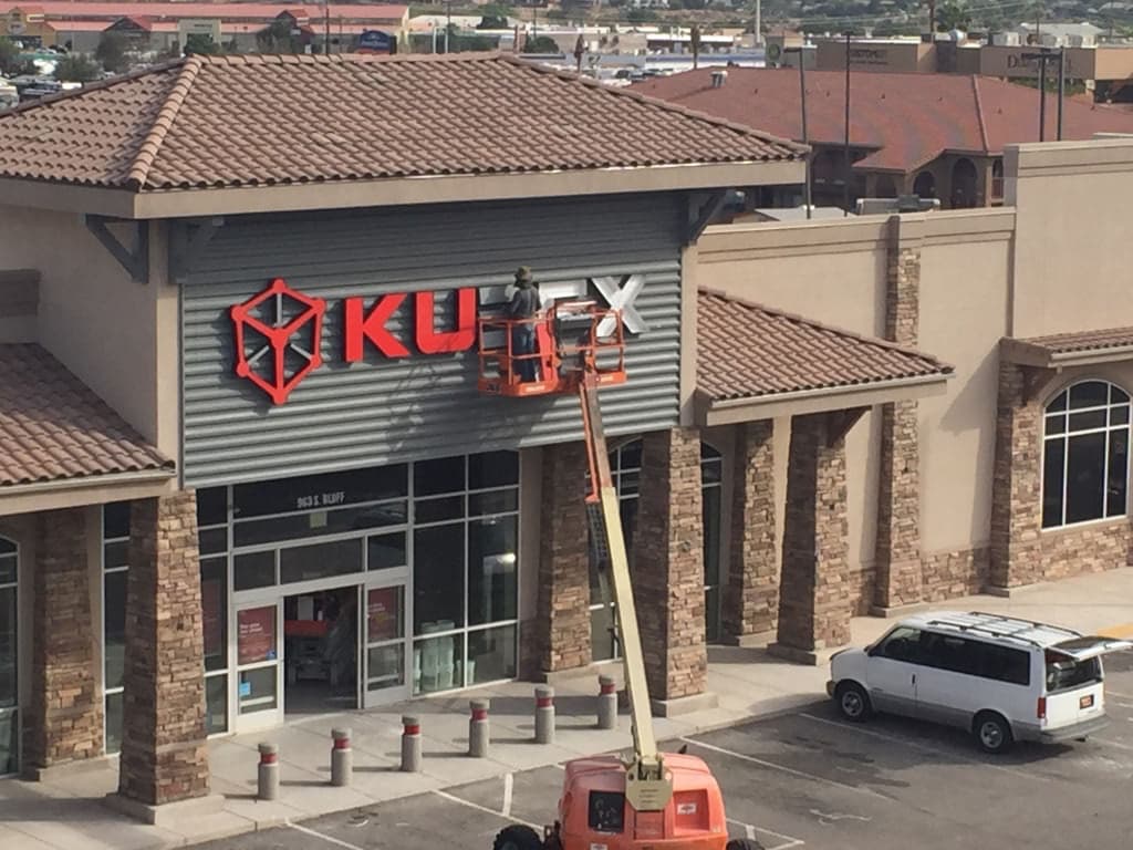 Technician using a lift to install an illuminated Kubex sign on a commercial building facade.
