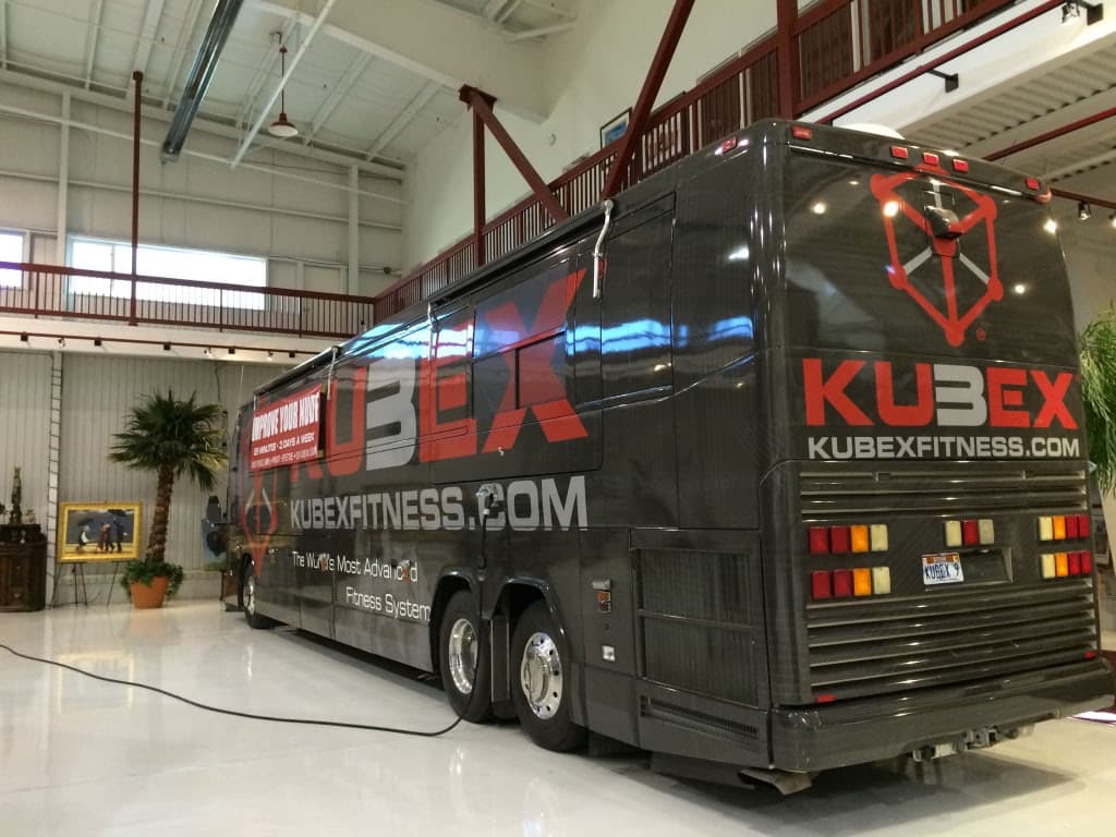 Large tour bus featuring a custom dark gray and red full vehicle wrap for Kubex Fitness.