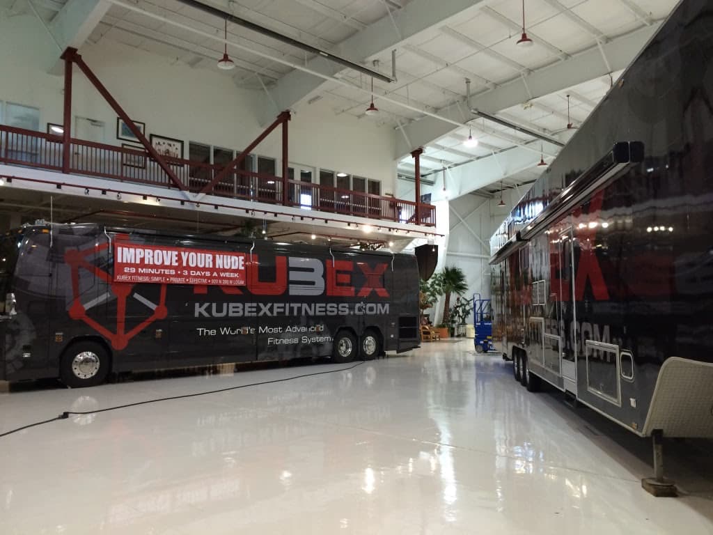 Two large buses wrapped with Kubex Fitness branding parked inside a spacious indoor garage.