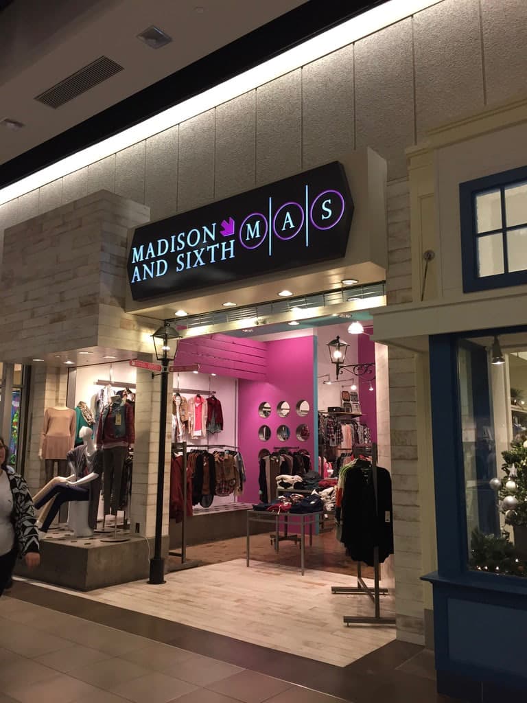 Illuminated Madison and Sixth store sign mounted above a retail boutique entrance inside a mall.