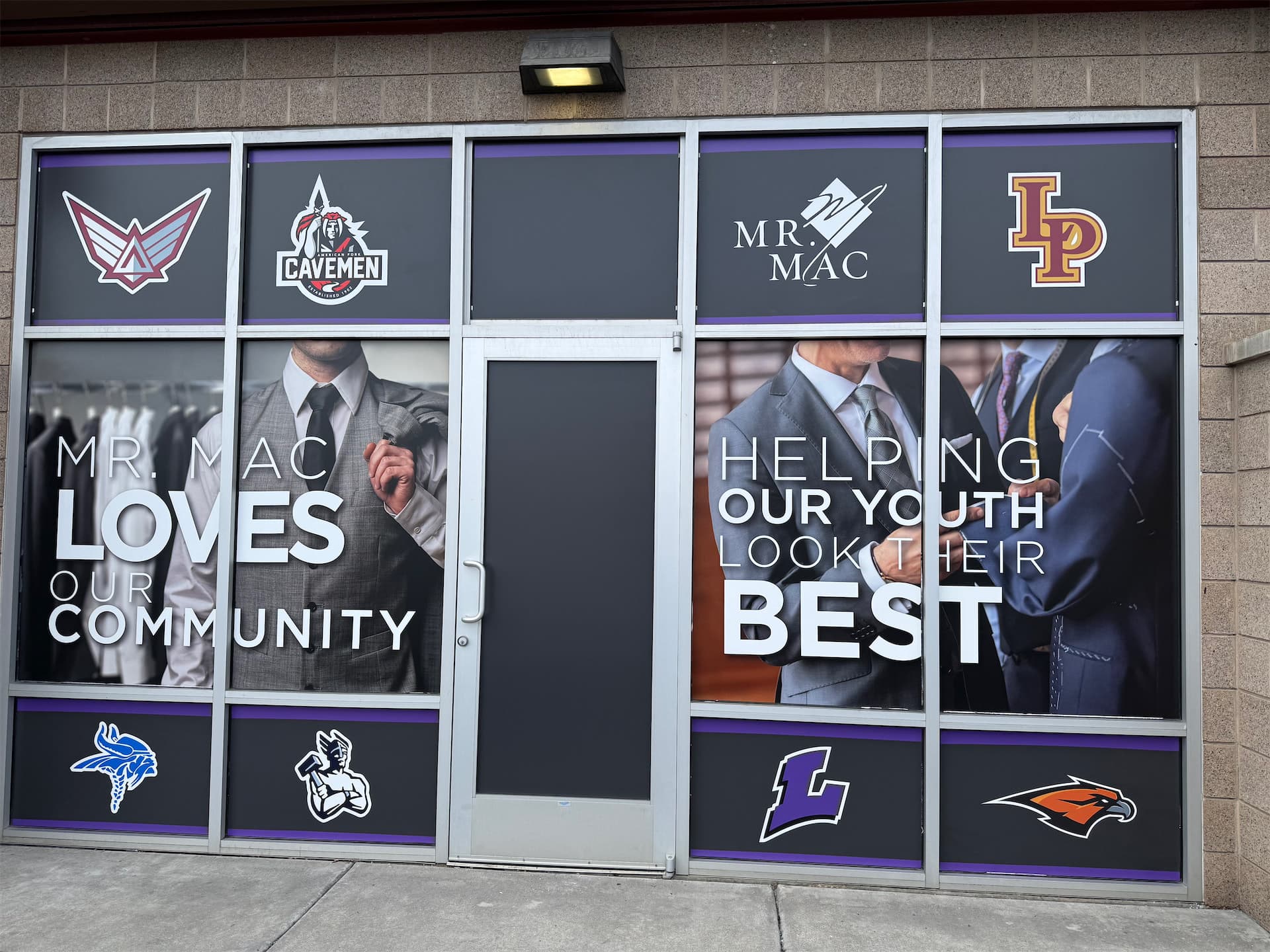 Storefront window graphics for Mr. Mac featuring community messaging and local high school logos.