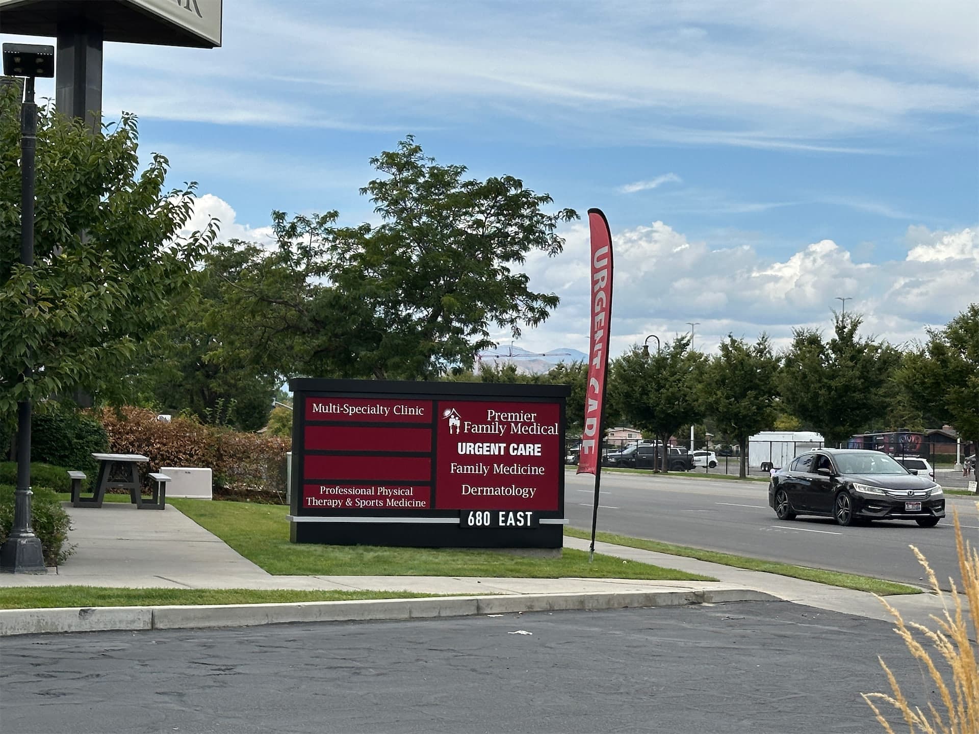 Premier Family Medical Urgent Care outdoor monument sign and red feather flag along a street.