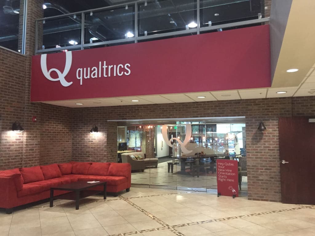 Qualtrics lobby sign featuring white dimensional logo and lettering on a large red fascia above entrance glass doors.