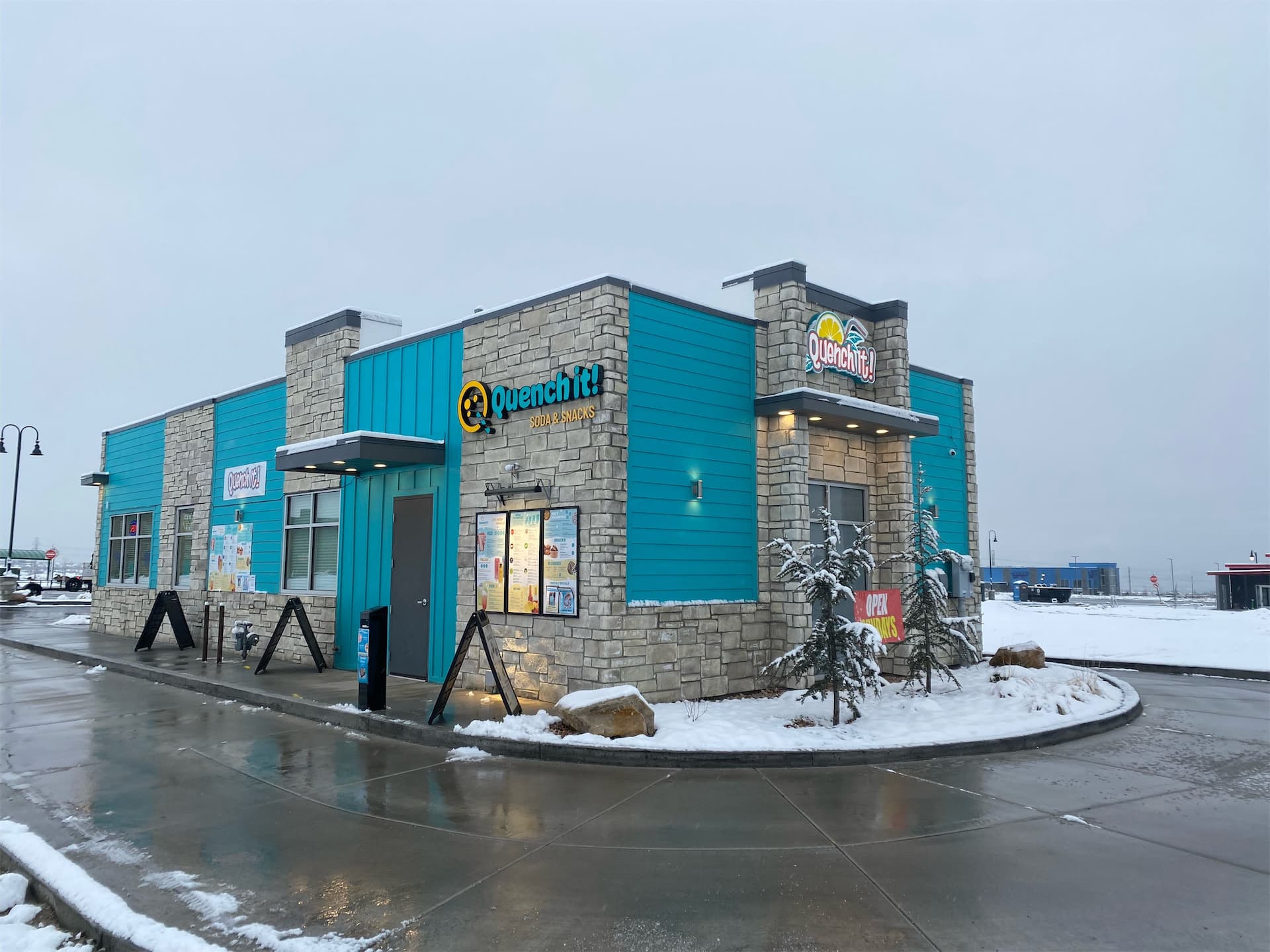Exterior view of Quench It Soda and Snacks building with illuminated building signage and stone facade.
