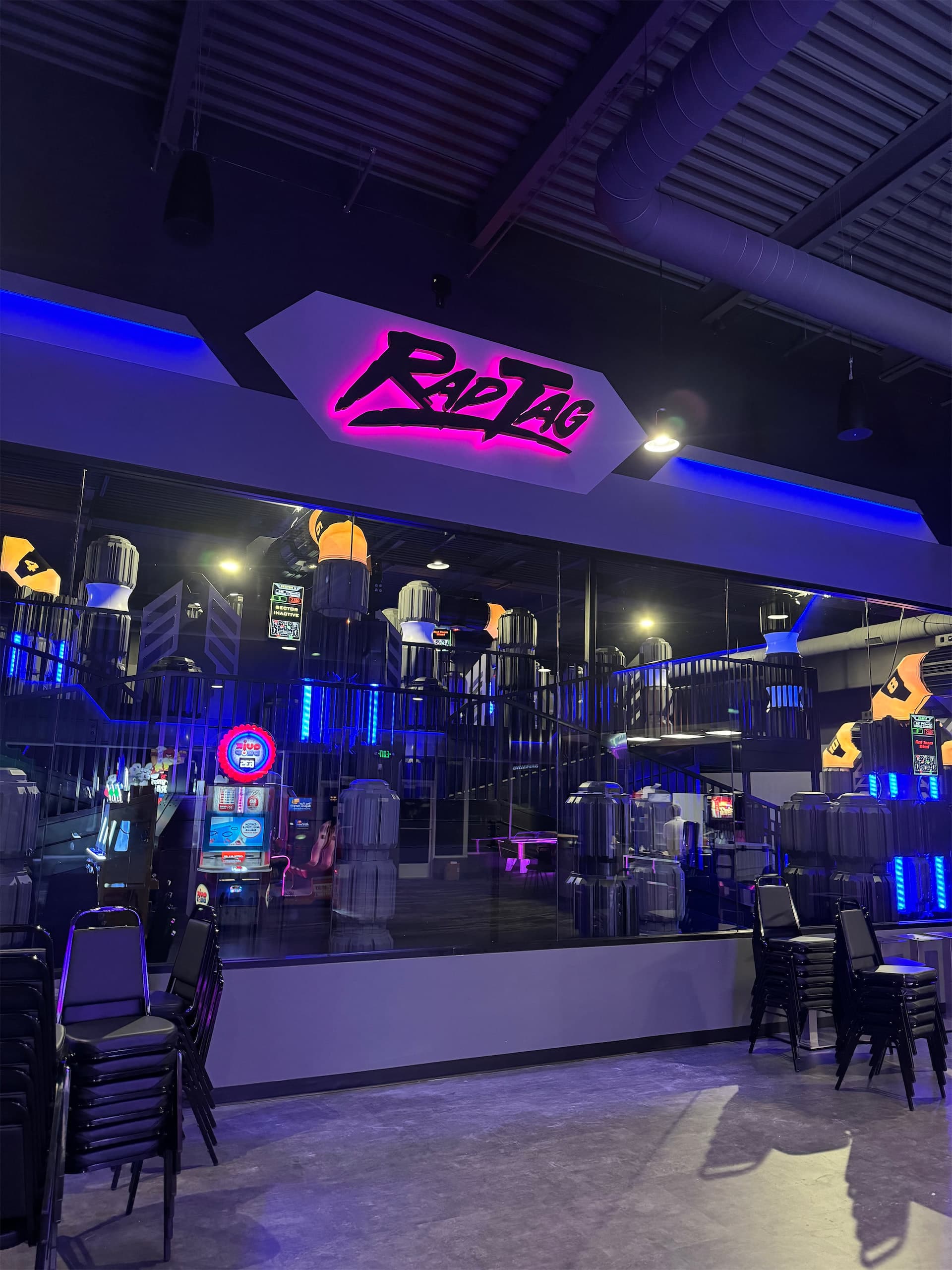 Pink illuminated Rad Tag electric sign inside a modern indoor laser tag arena with blue accent lights.