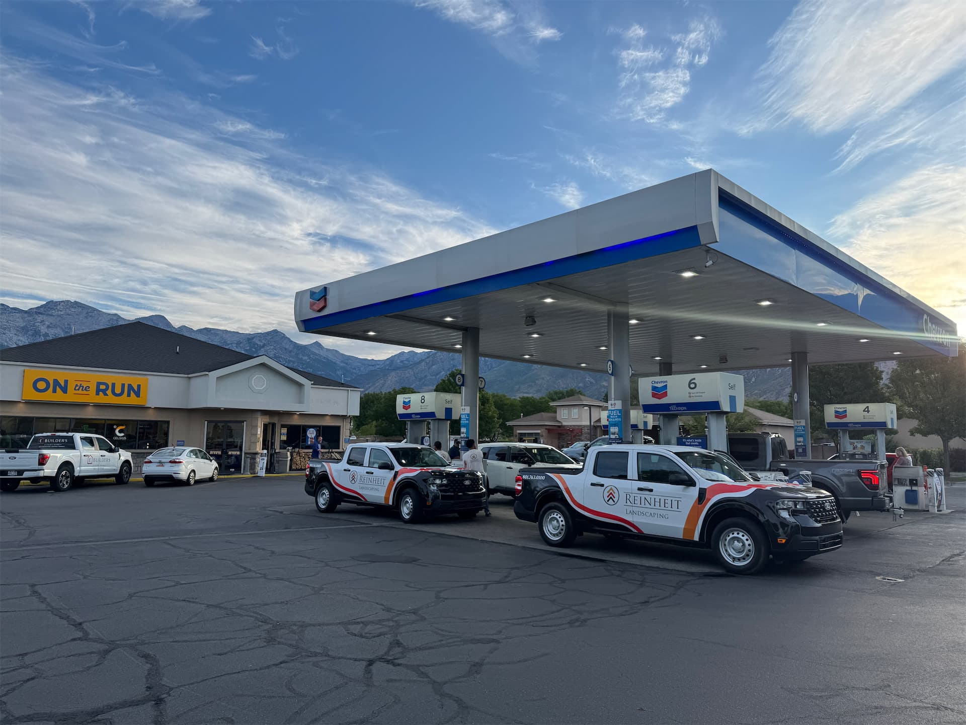 Two Reinheit Landscaping pickup trucks with custom vehicle wraps parked at a gas station.