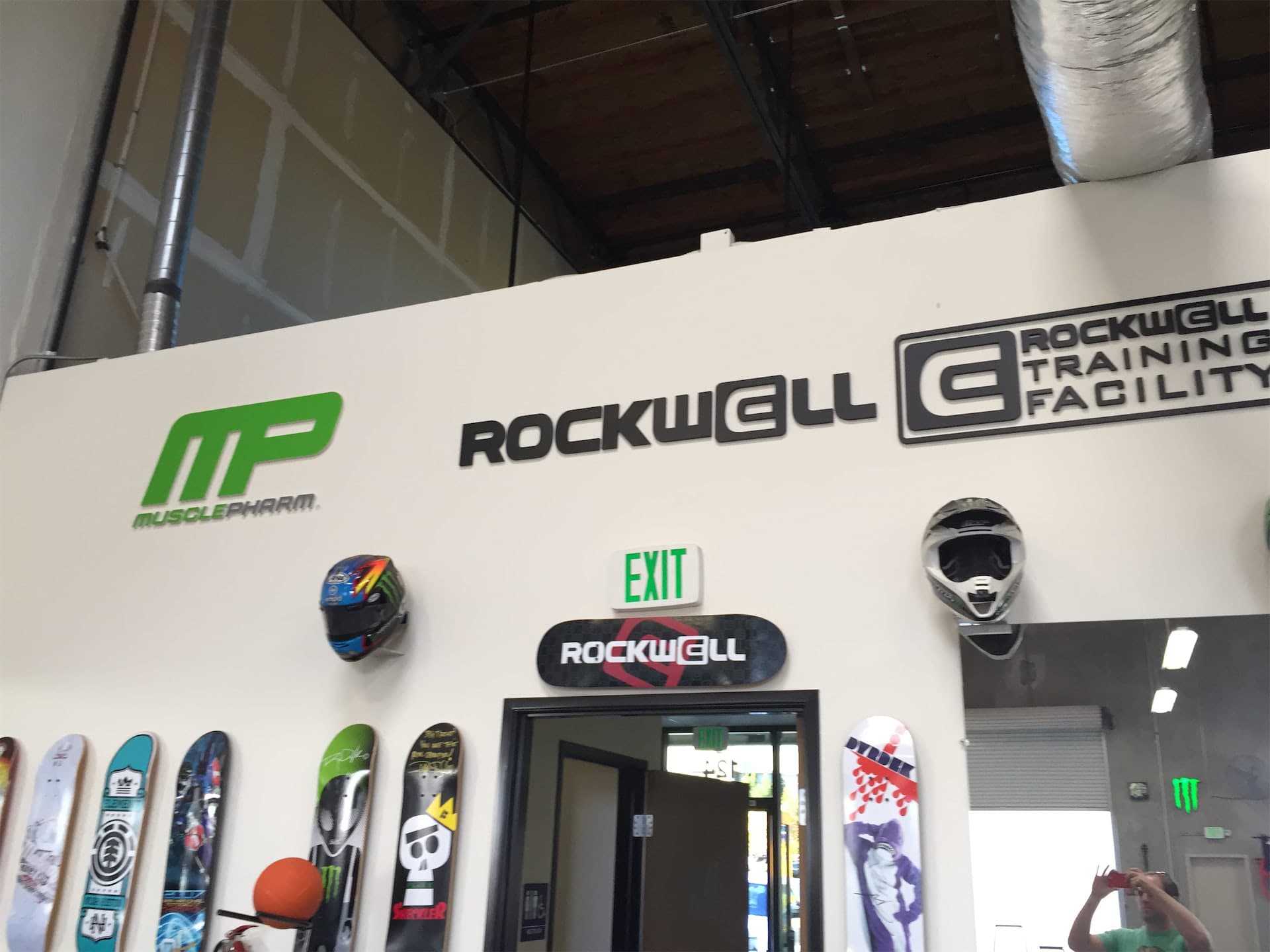 Rockwell and MusclePharm custom 3D lobby signs displayed on a wall with mounted skateboards and helmets.