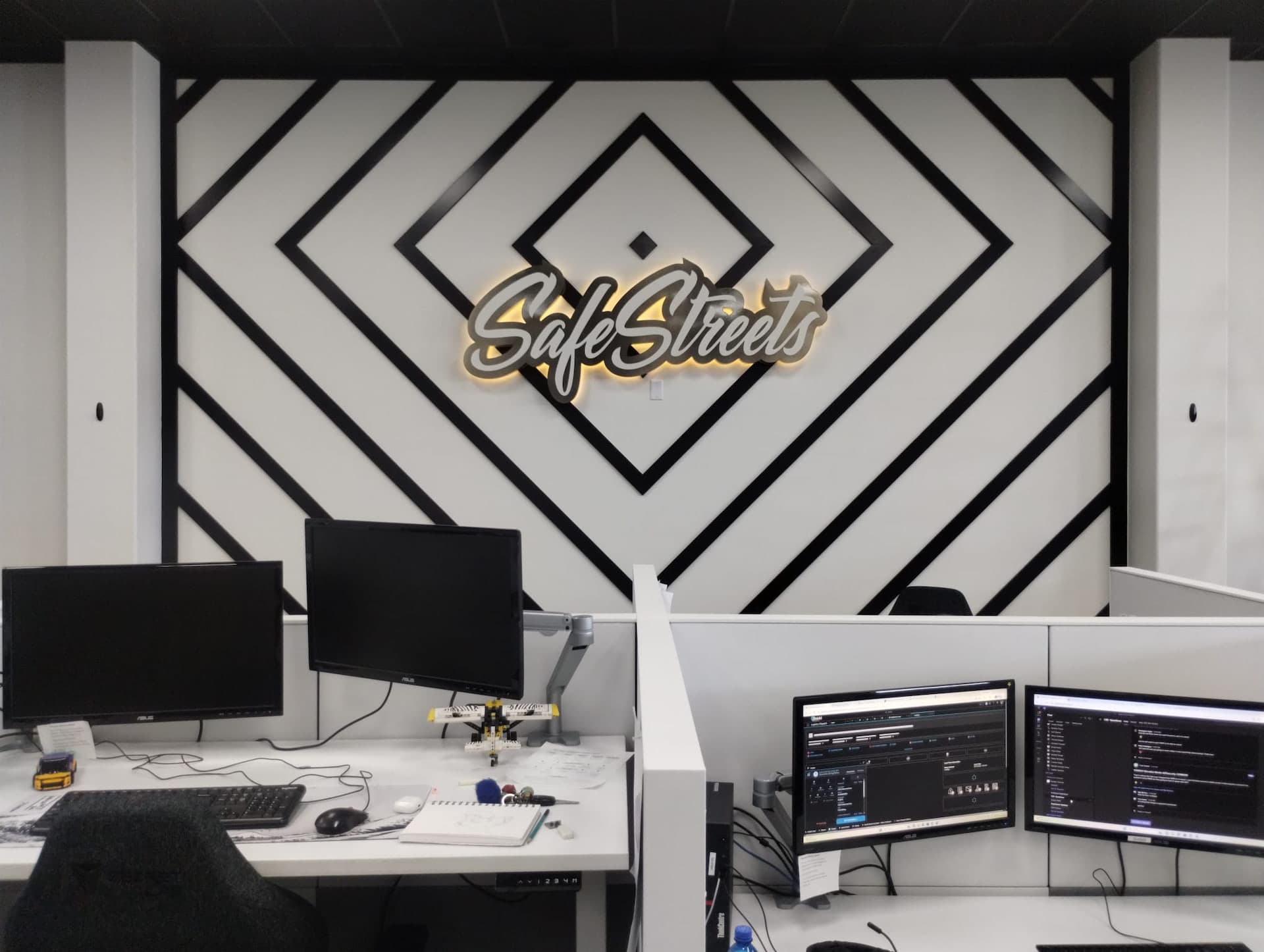 Backlit SafeStreets logo mounted on a geometric accent wall above office desks.