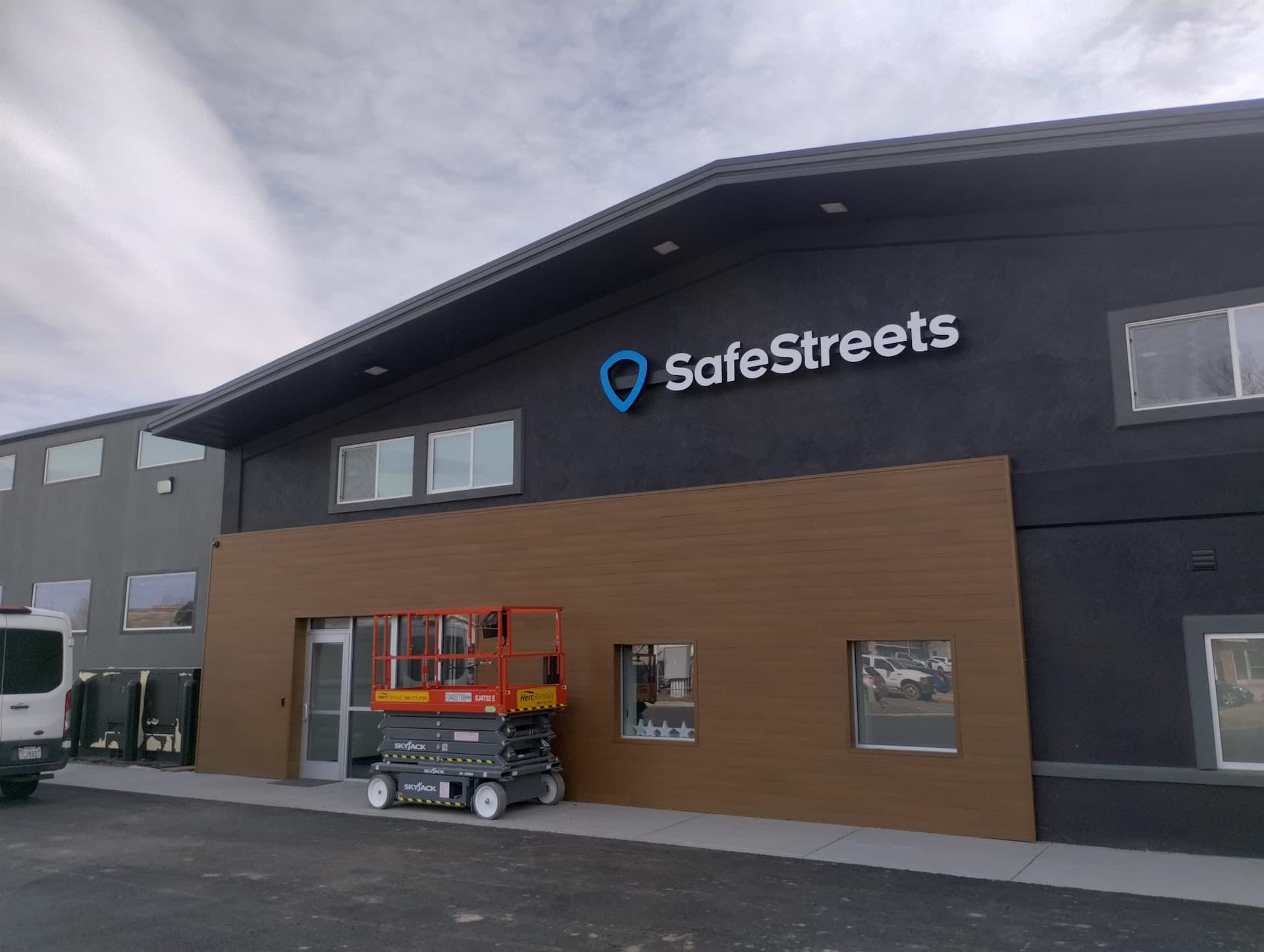 Exterior illuminated SafeStreets sign mounted on a modern dark gray building with wood paneling.