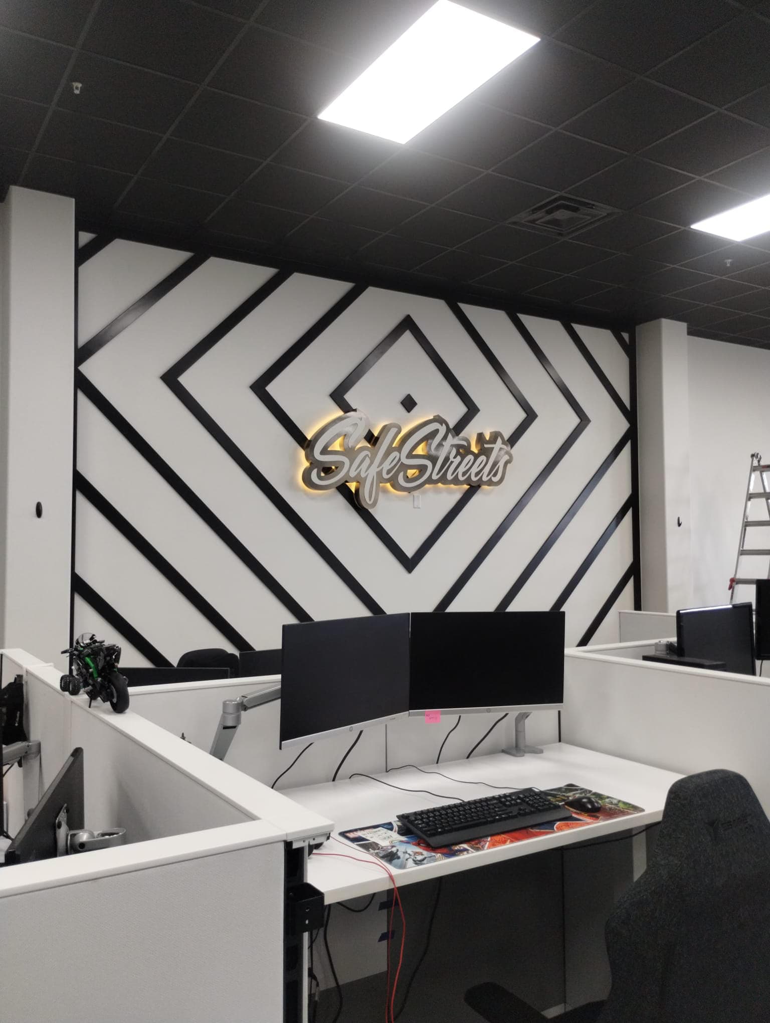 Backlit SafeStreets logo mounted on a black and white geometric feature wall in an office environment.