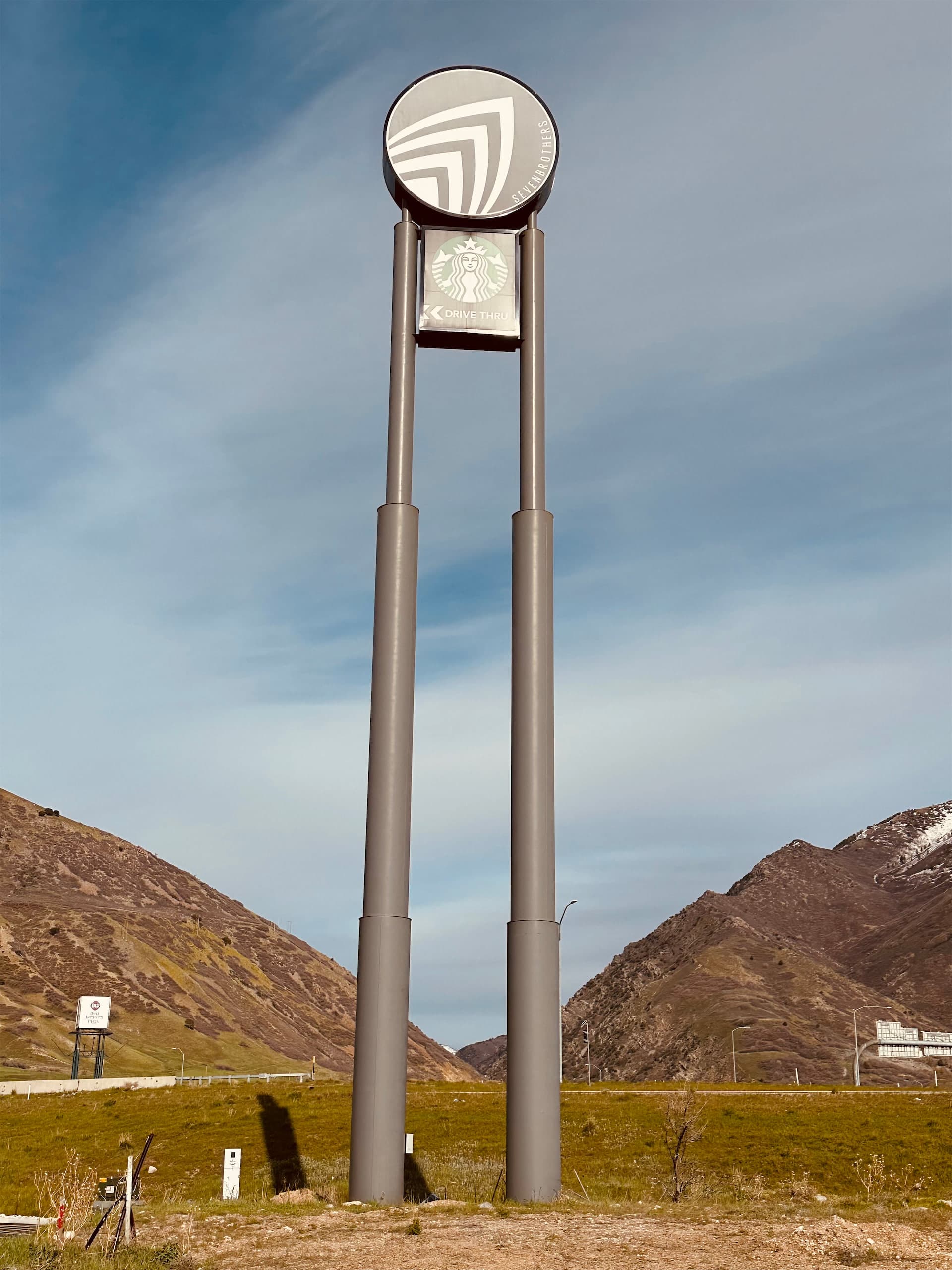 A tall outdoor pylon sign featuring Seven Brothers and Starbucks logos set against a mountain backdrop.