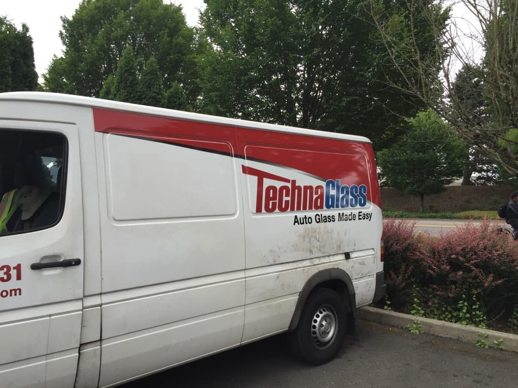 Side view of a TechnaGlass service van featuring a red and blue custom vehicle wrap.