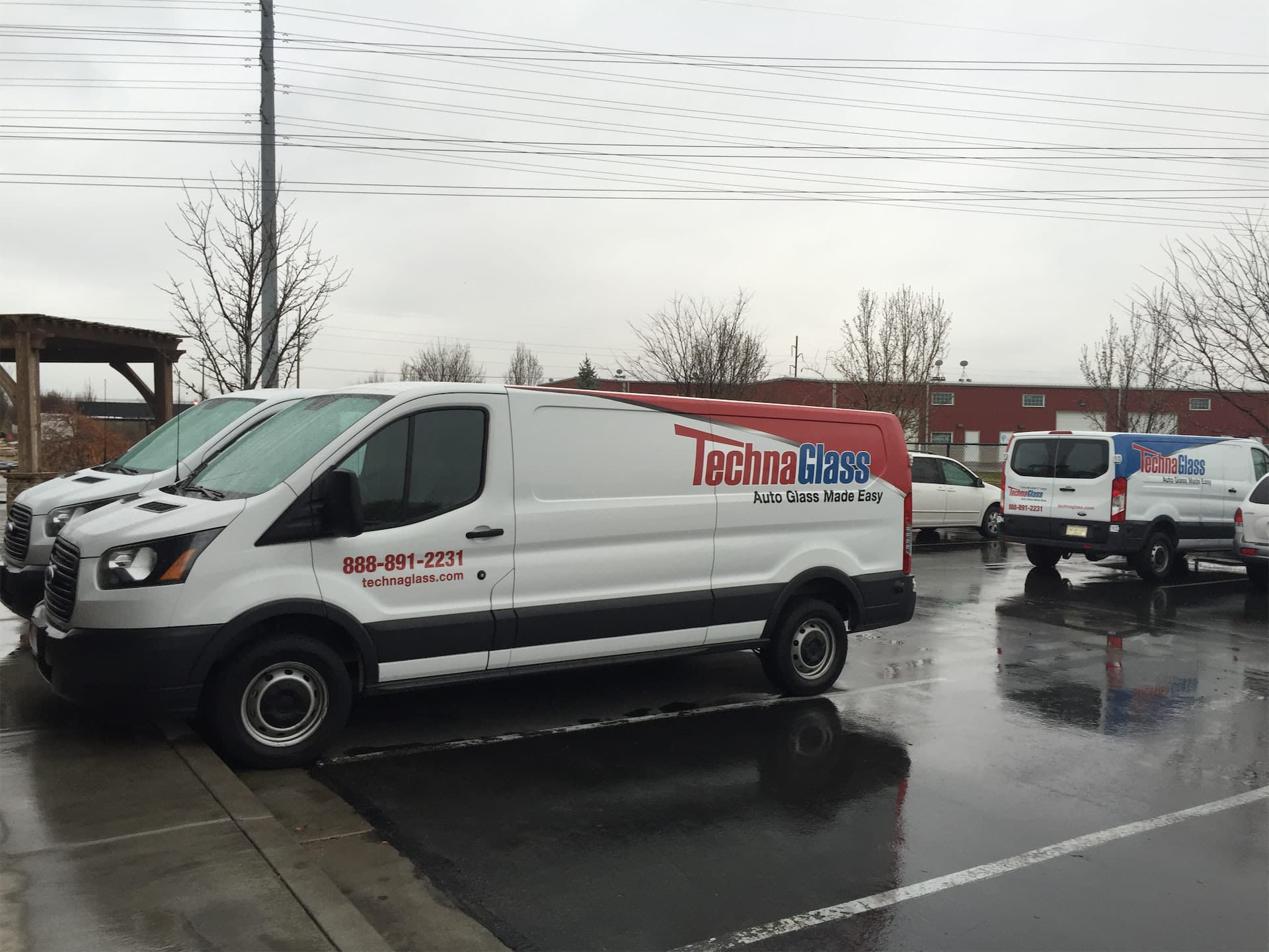 White TechnaGlass commercial van with custom vinyl vehicle wrap parked in a lot.