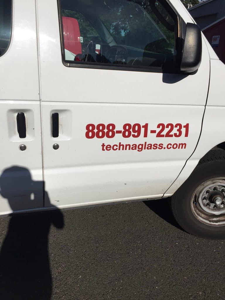 Side door of a white van with red vinyl decal lettering displaying a phone number and website.