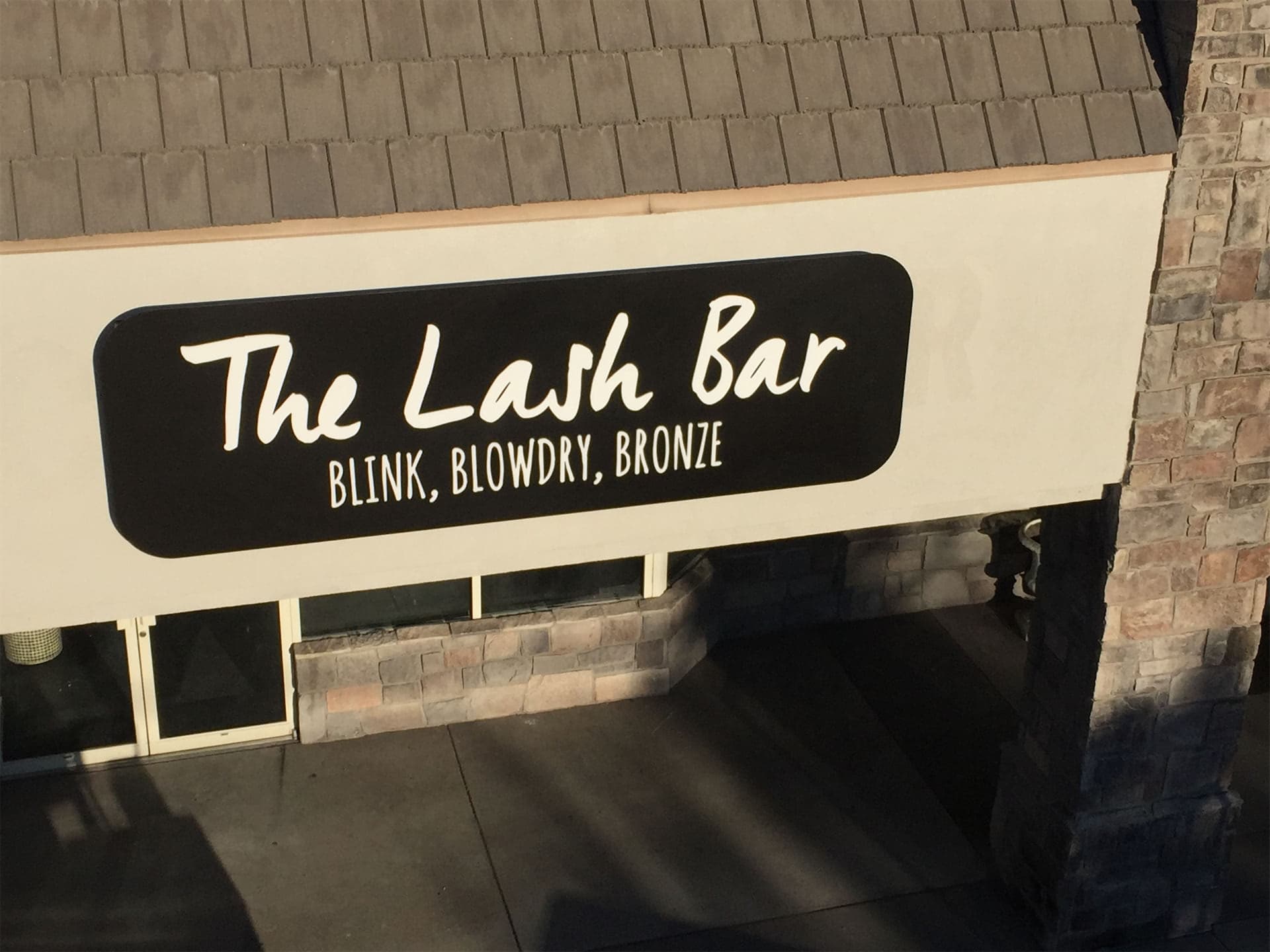 Exterior black storefront sign for The Lash Bar with white lettering mounted on a building facade.